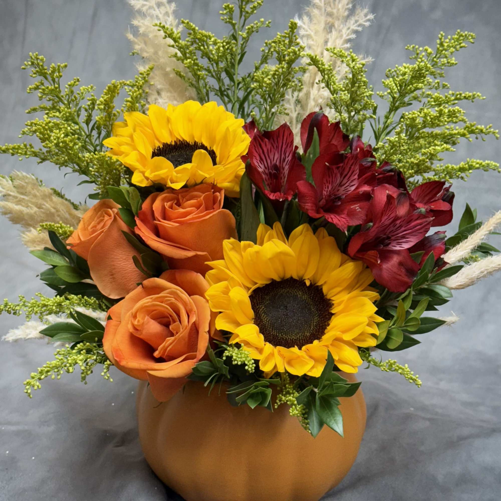 Orange roses and sunflowers in a pumpkin-shaped vase with red alstroemeria