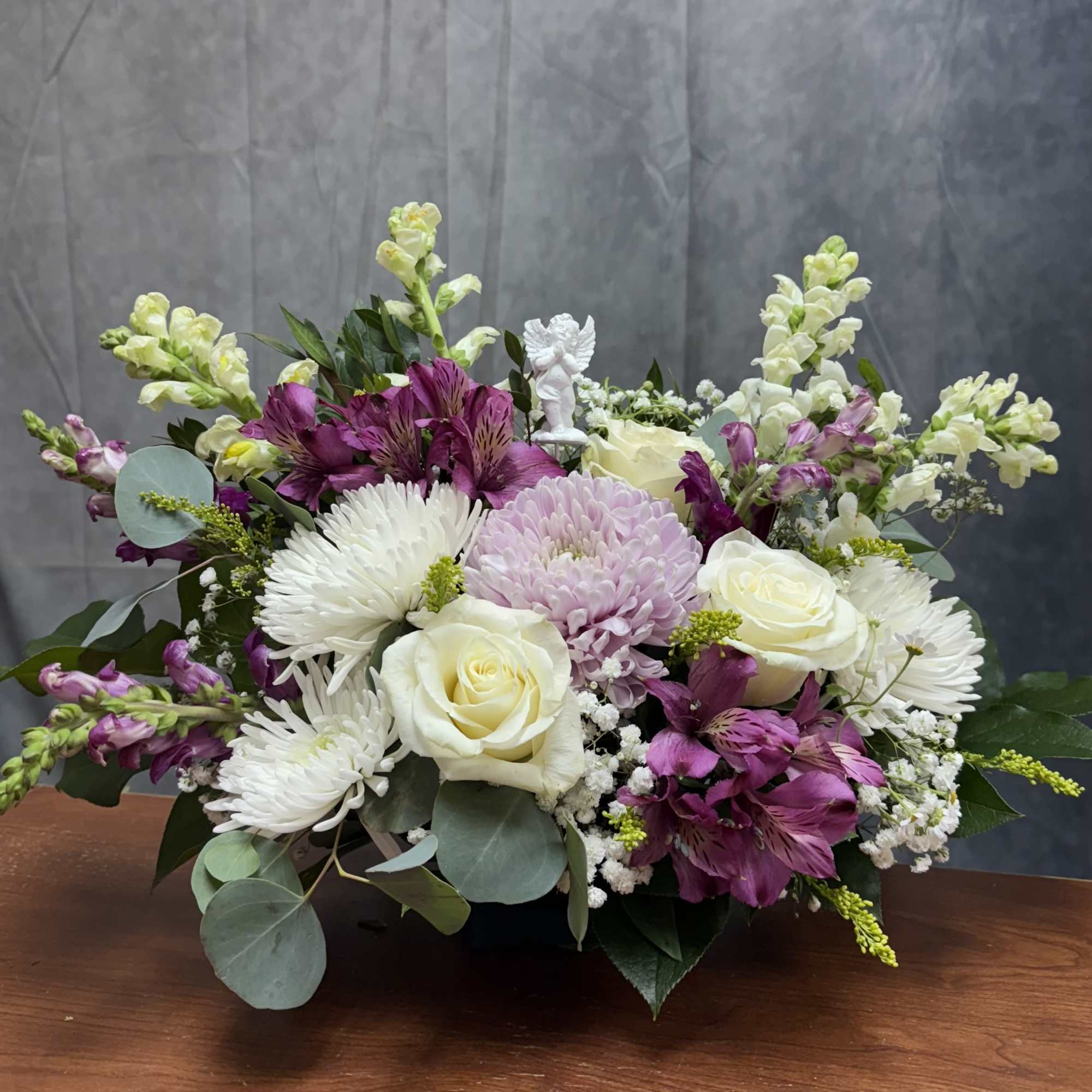 Mixed bouquet of white roses, purple flowers, and white daisies in a low container