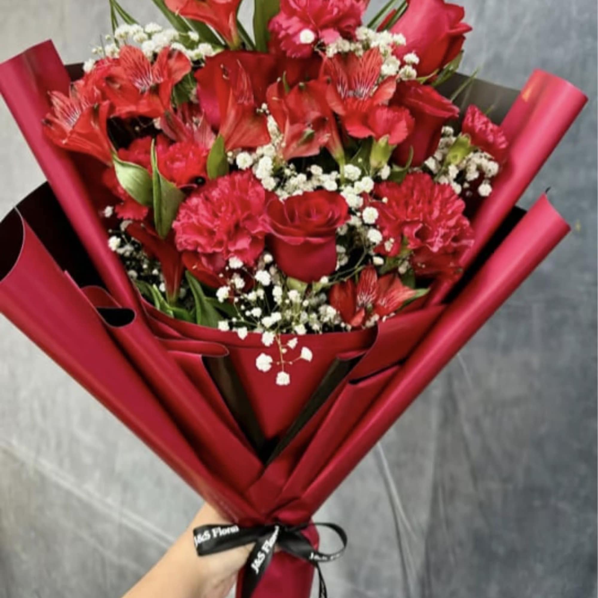 A romantic hand-tied bouquet featuring rich red roses, carnations, and alstroemeria, delicately