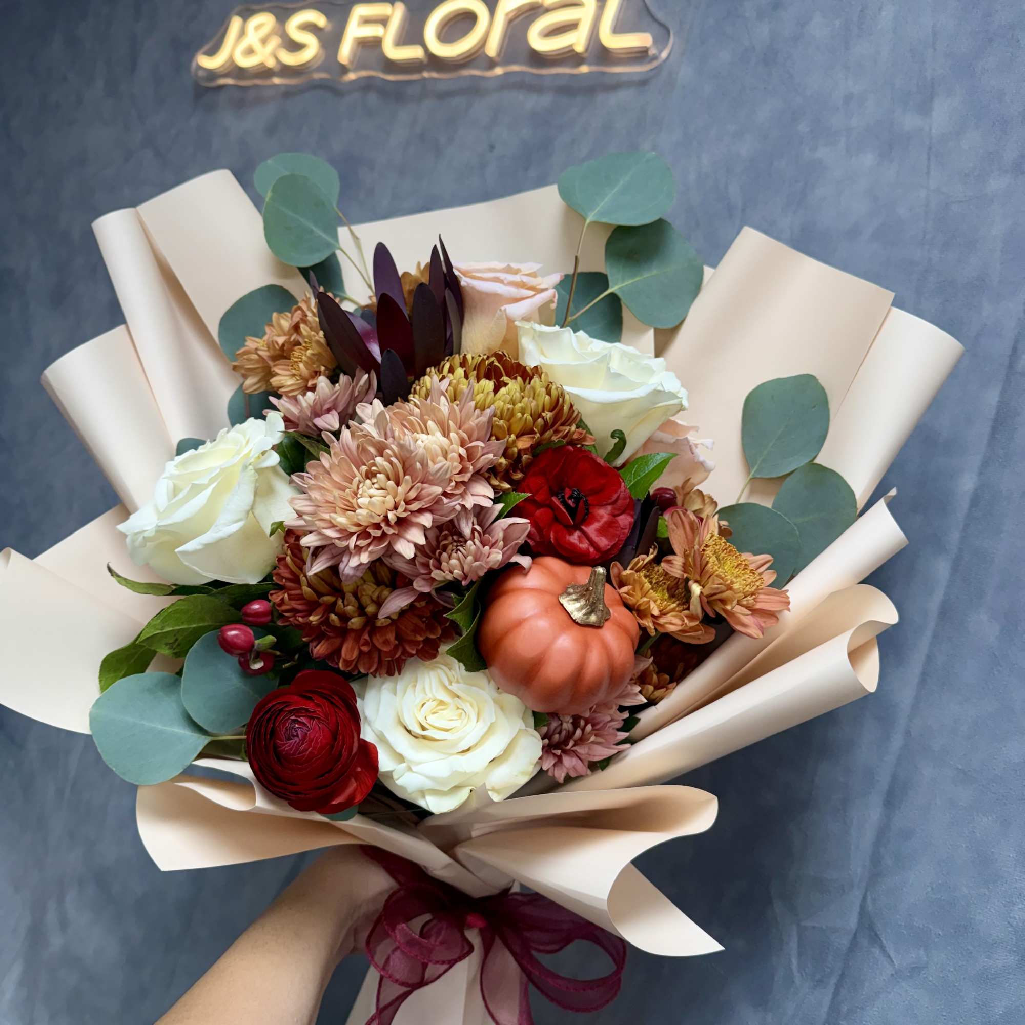 Hand-tied bouquet of roses, chrysanthemums, and a small pumpkin wrap