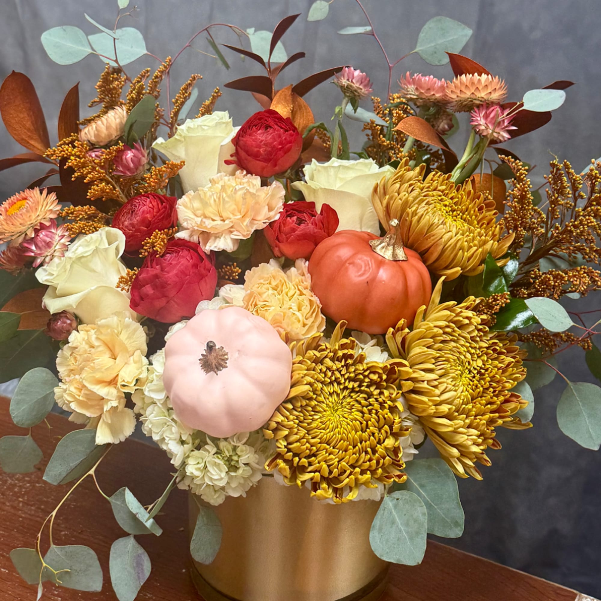 Autumn floral arrangement with chrysanthemums, roses, and small pumpkins in a gold vase
