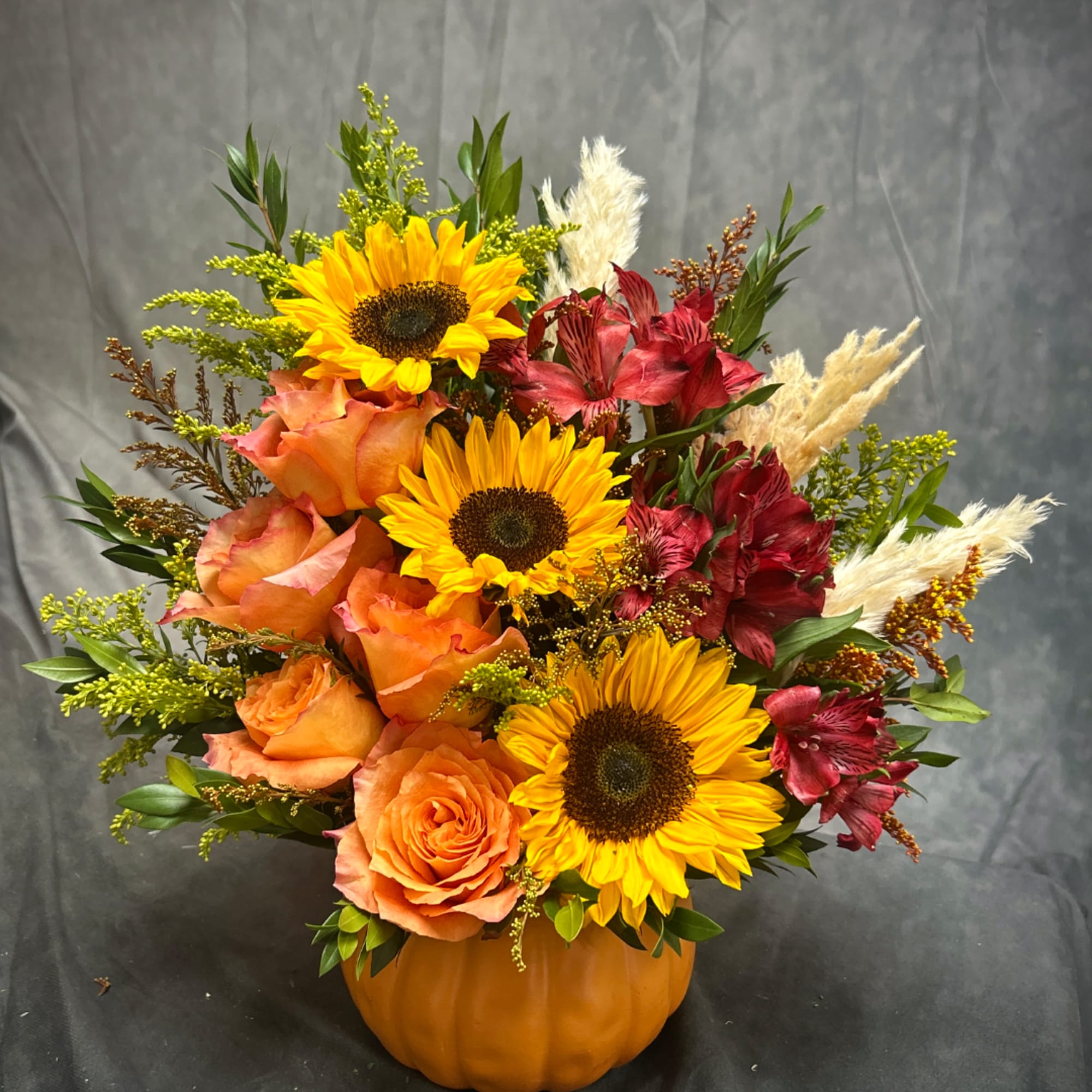 Autumn bouquet of sunflowers, orange roses, and red alstroemeria in a pumpkin vase