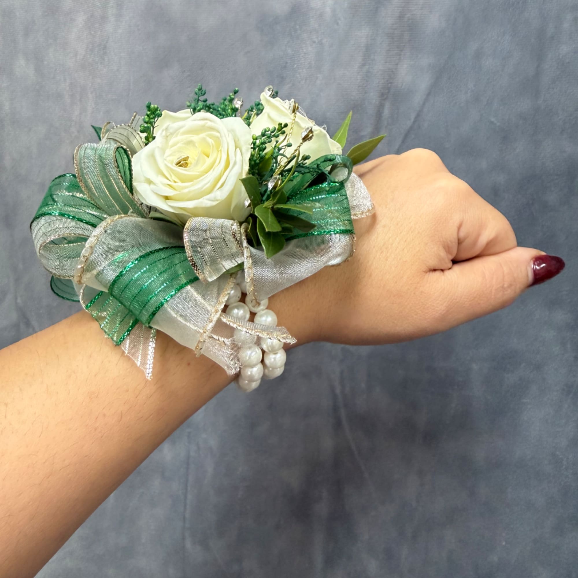White rose wrist corsage with green ribbon and pearl accents on a person's wrist
