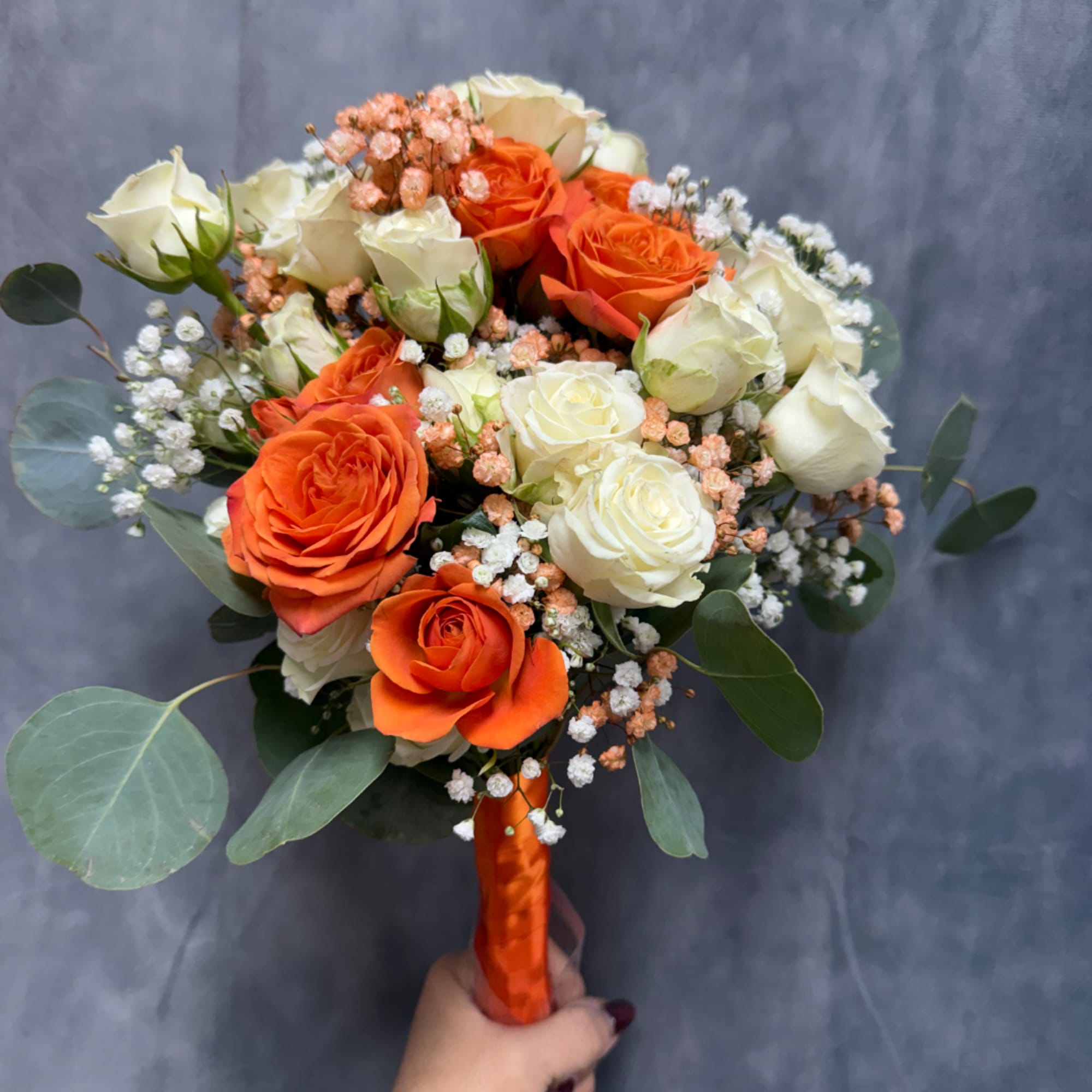 Handheld bouquet of orange and white roses with baby's breath