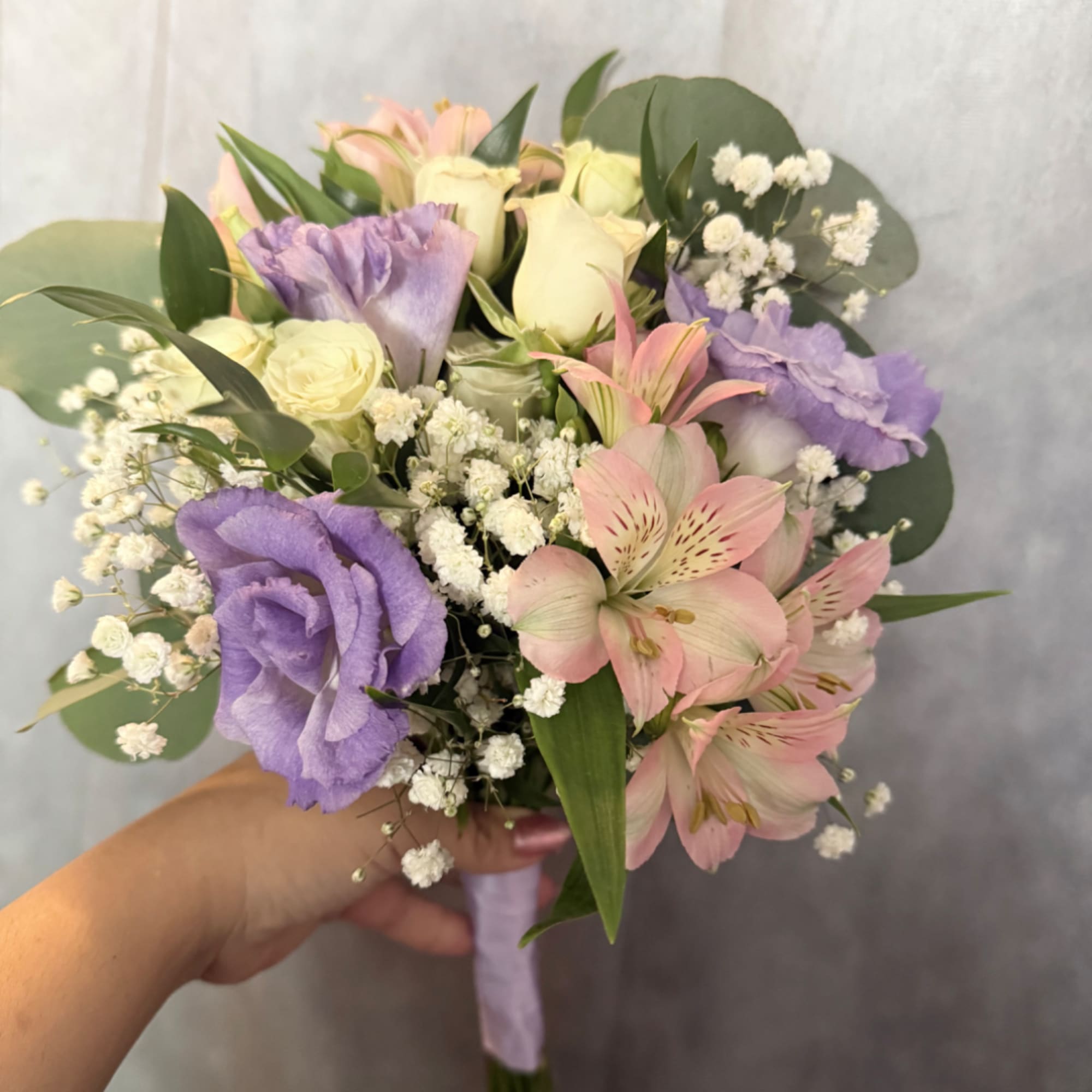 Handheld bouquet of pink and purple flowers with white filler blooms