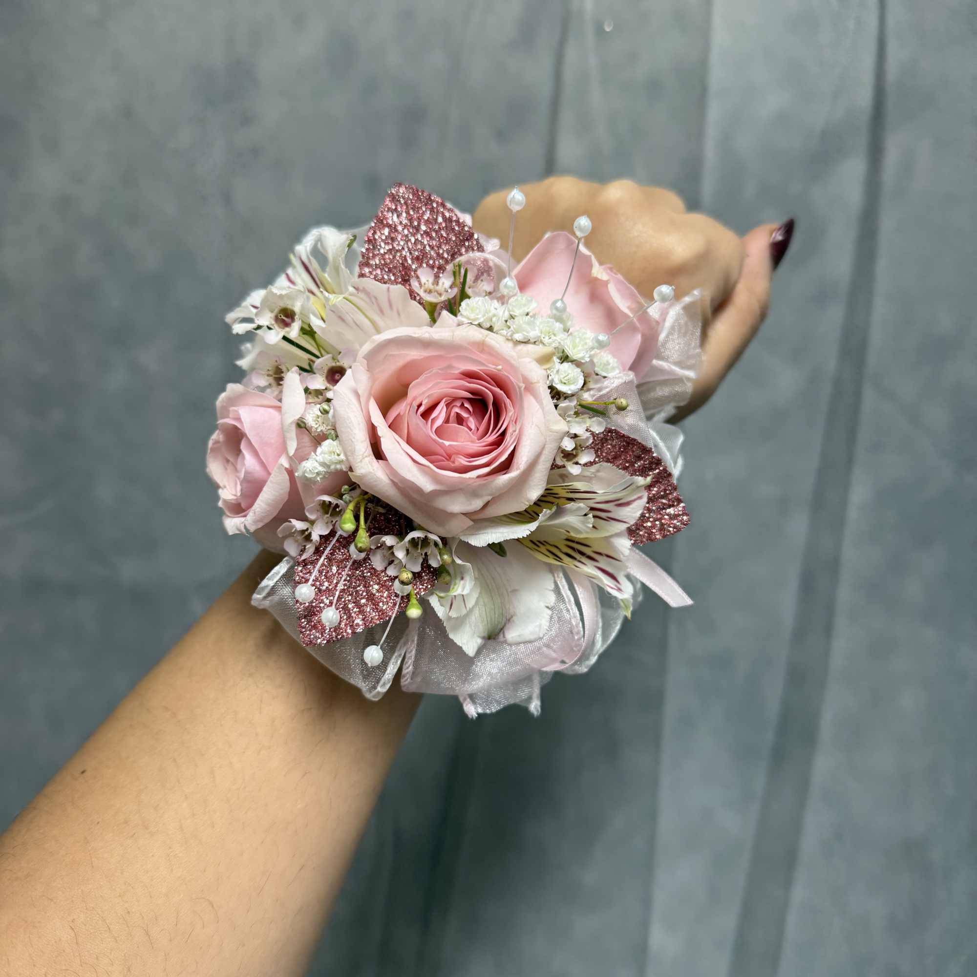 Small pink rose corsage with white accents worn on a wrist
