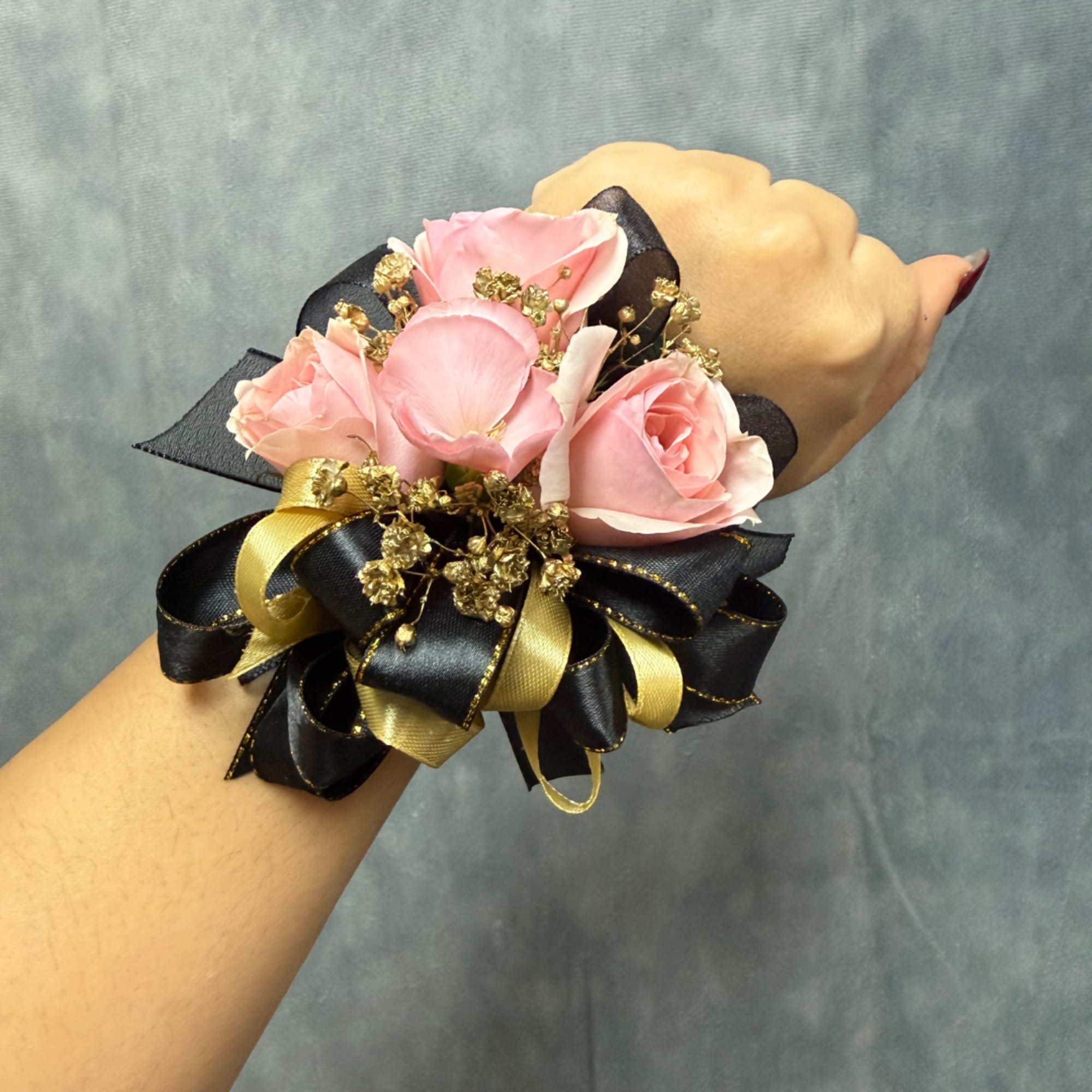 Pink rose wrist corsage with black and gold ribbon on a person's wrist, photo 2 of 3