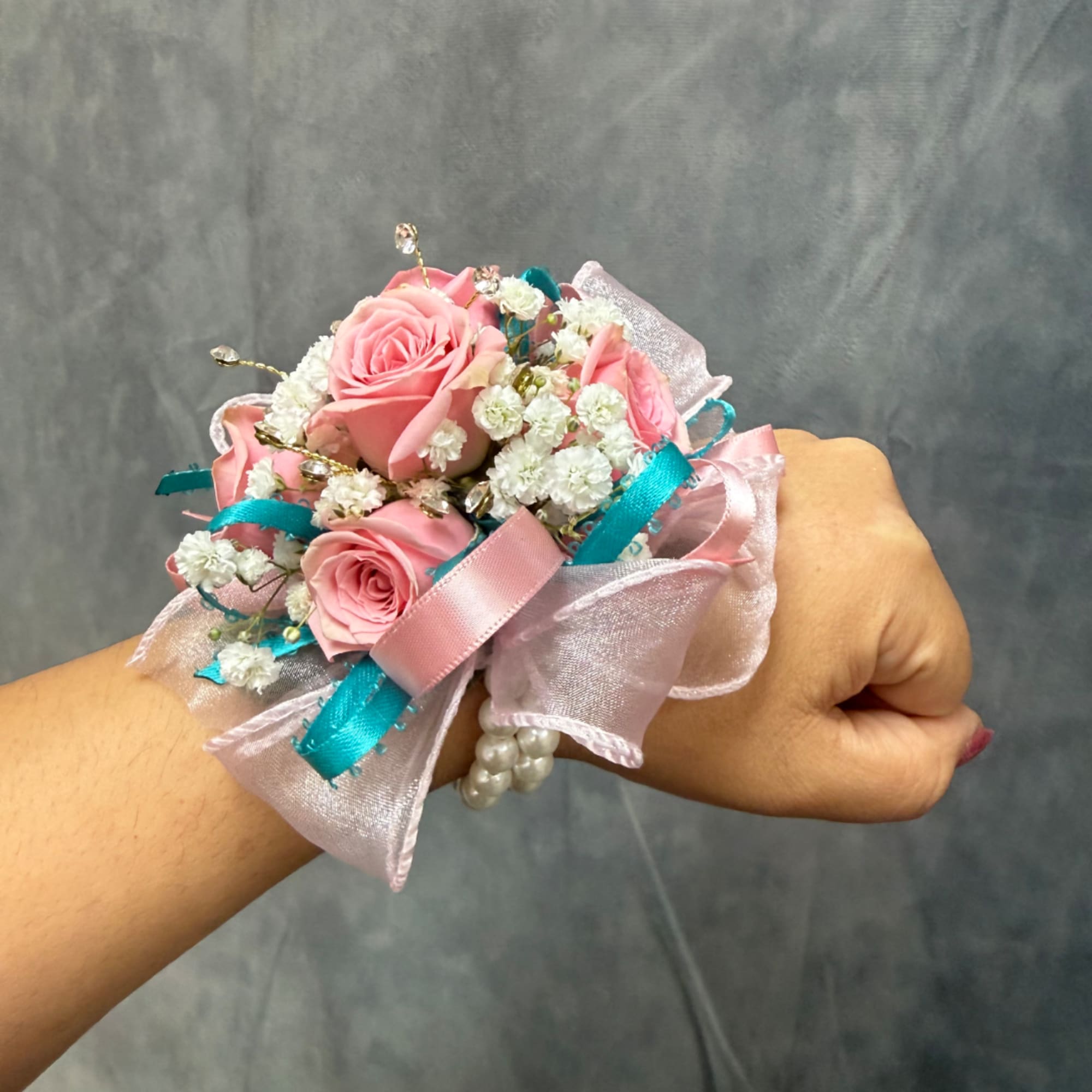 Pink rose wrist corsage with white filler flowers and ribbon on a wrist
