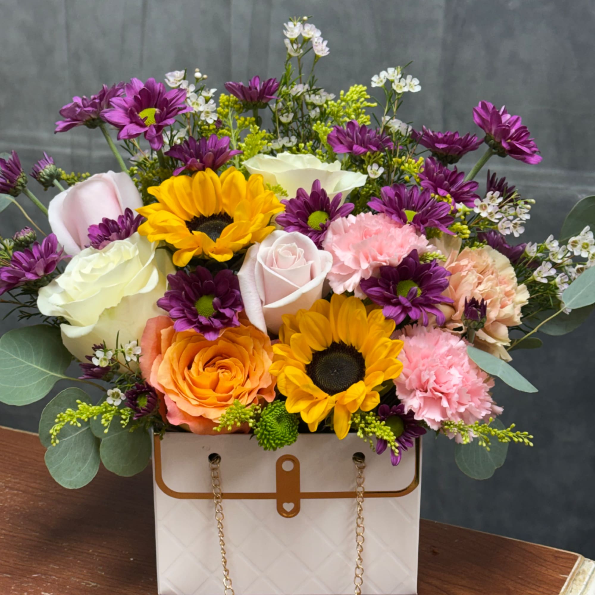 Mixed bouquet in a white handbag-style box with roses, sunflowers, and daisies