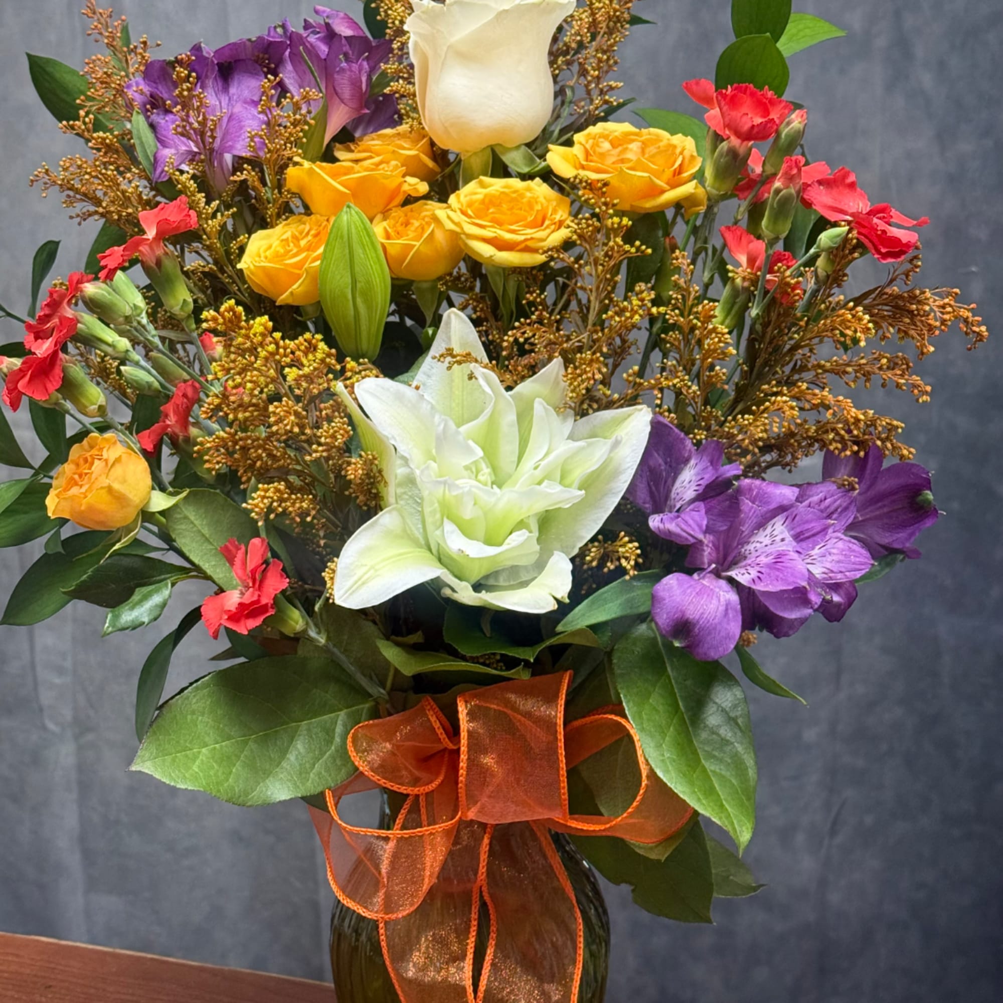 Colorful mixed bouquet in a glass vase with roses, lilies, and carnations