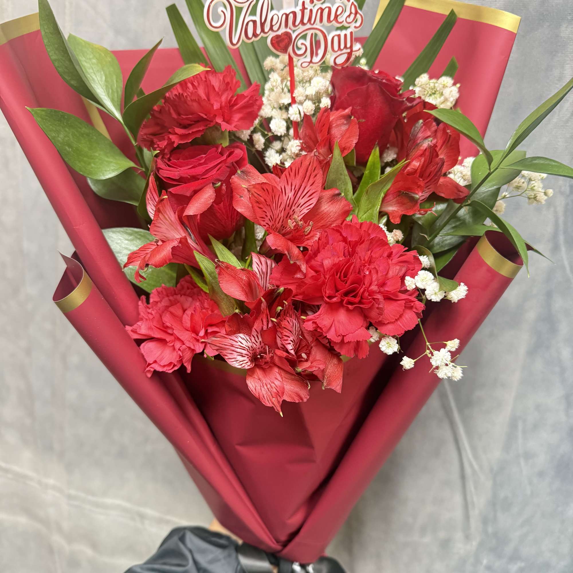 A romantic hand-tied bouquet featuring rich red roses, carnations, and alstroemeria, delicately