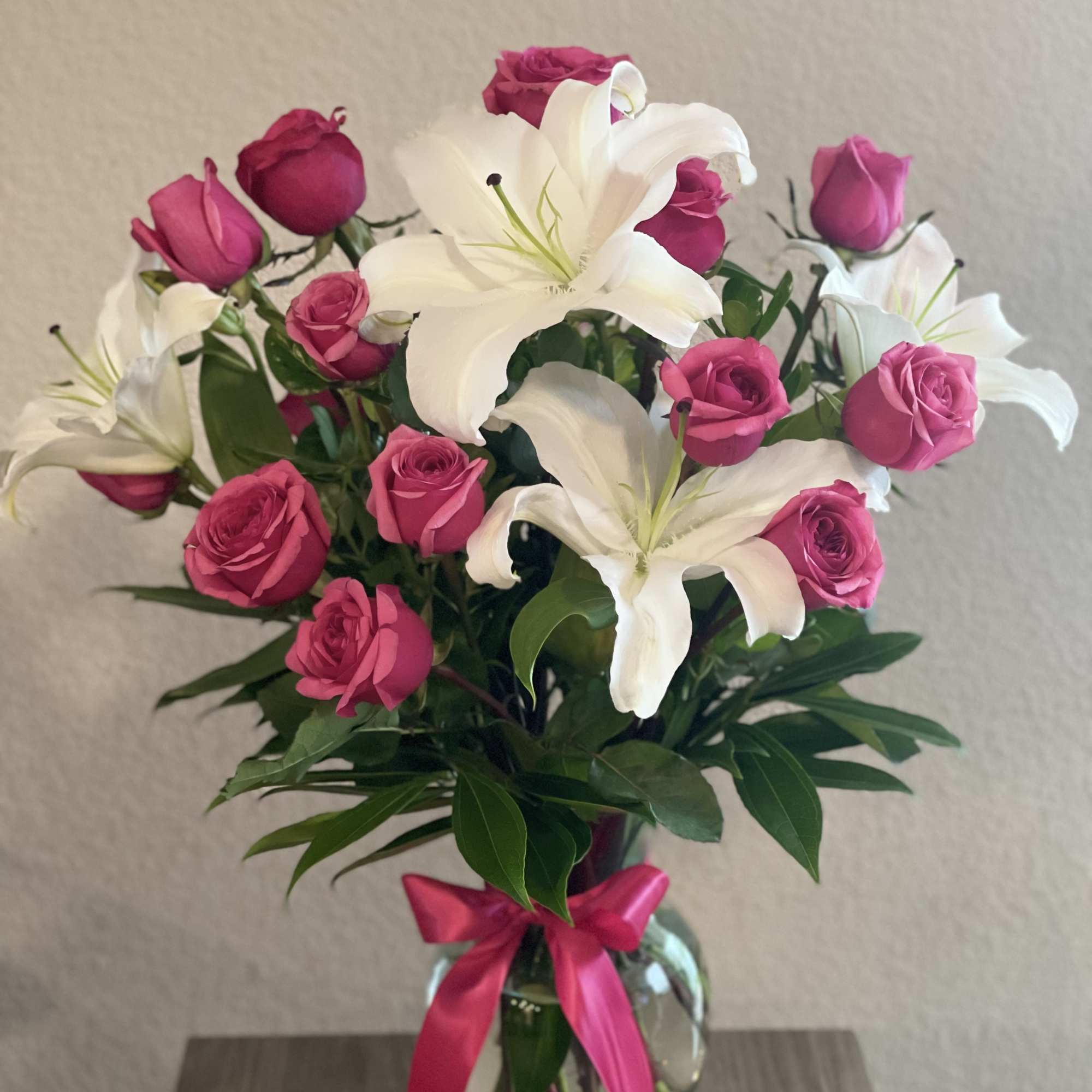 Pink roses and white lilies in a glass vase with a pink ribbon