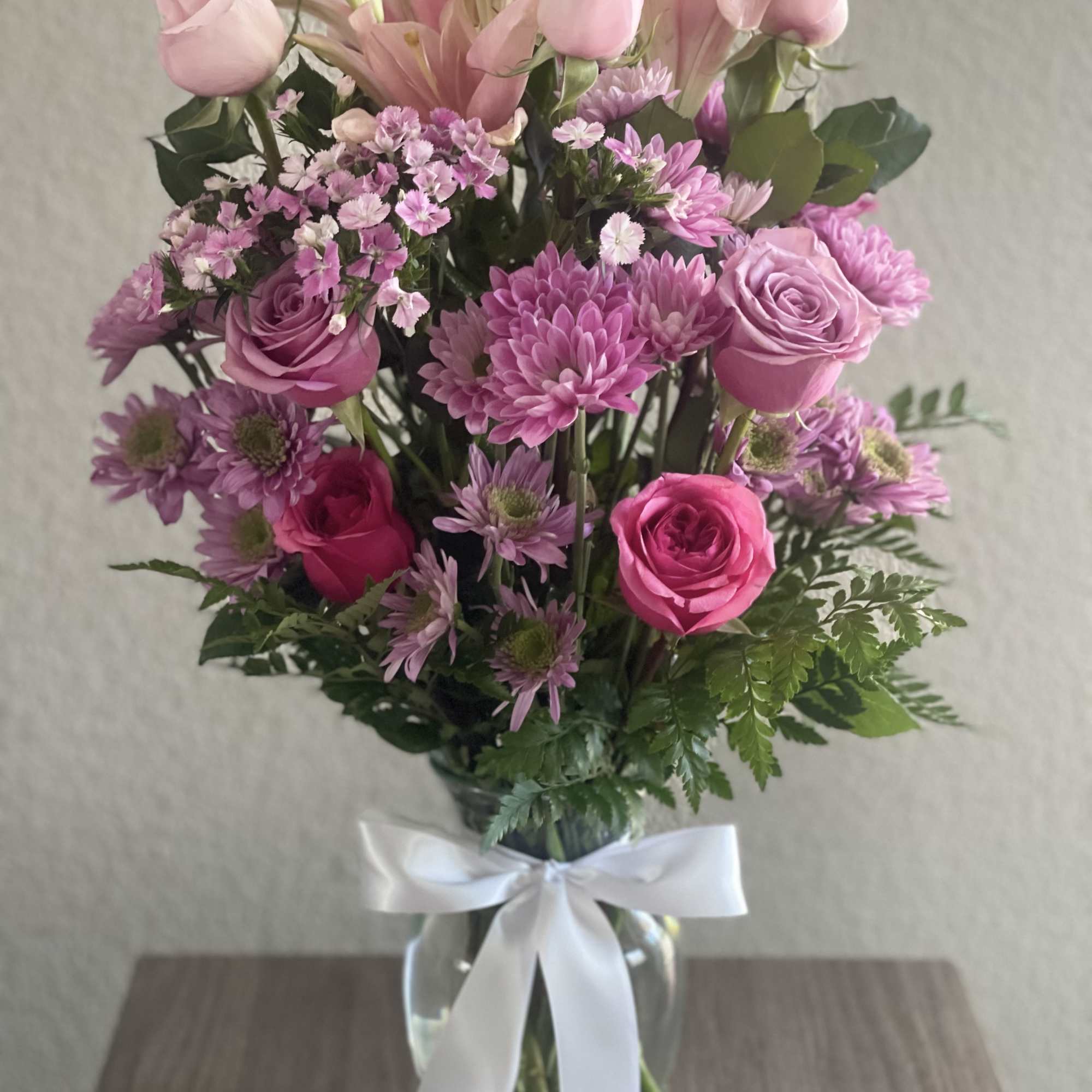 Pink roses and lilies arranged in a glass vase with a white ribbon