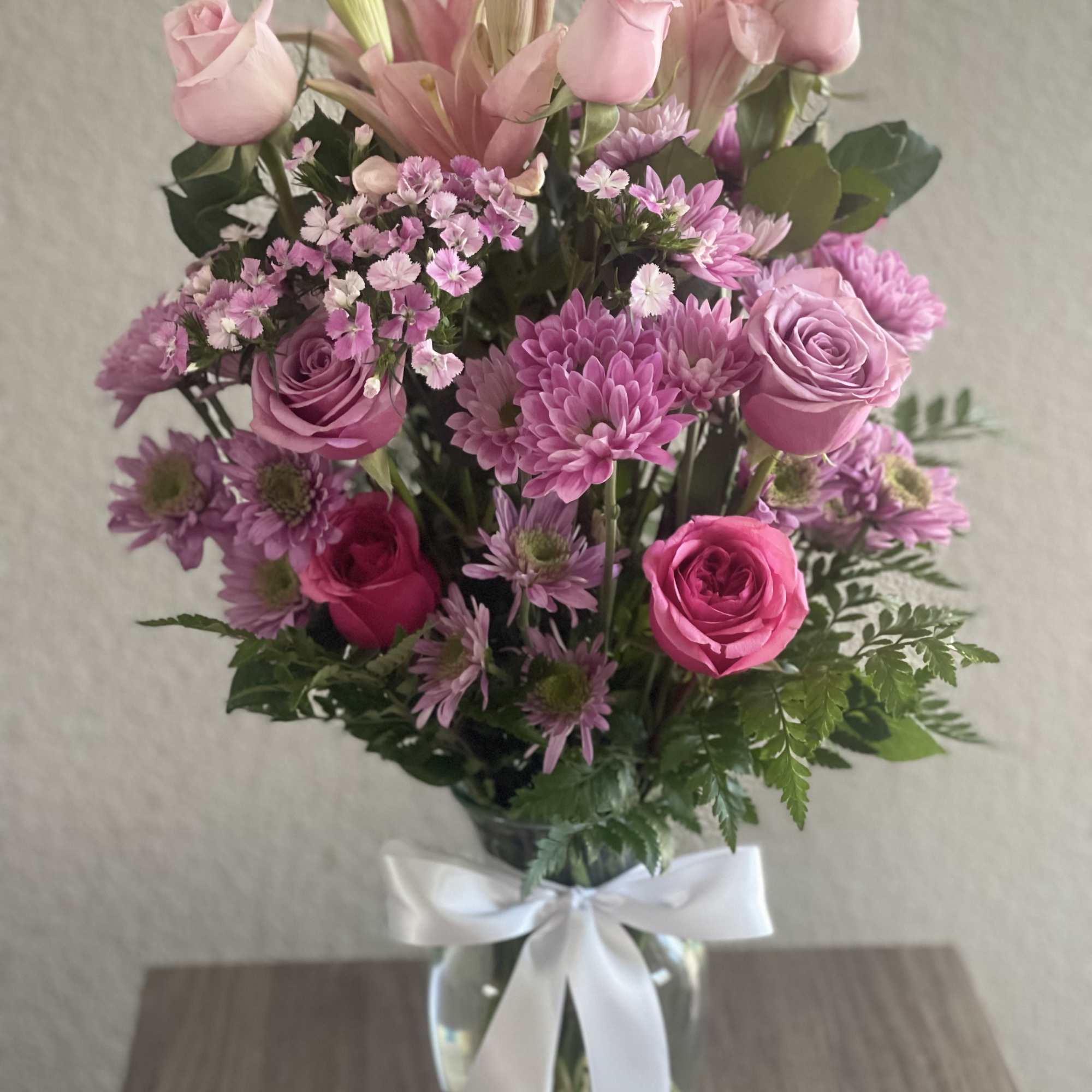 Pink roses and lilies in a glass vase with a white ribbon
