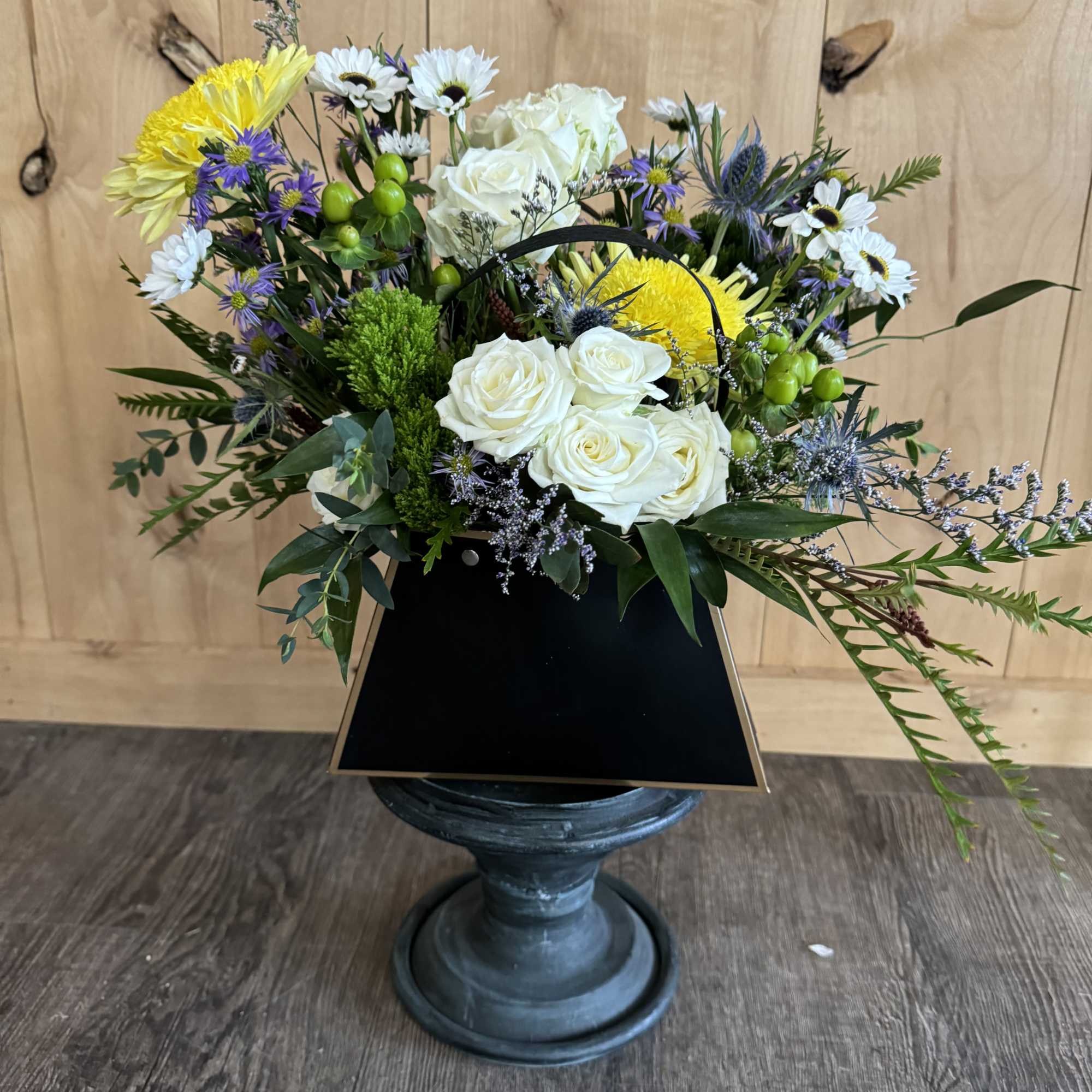 Mixed bouquet of white roses, yellow chrysanthemums, and small daisies in a black vase