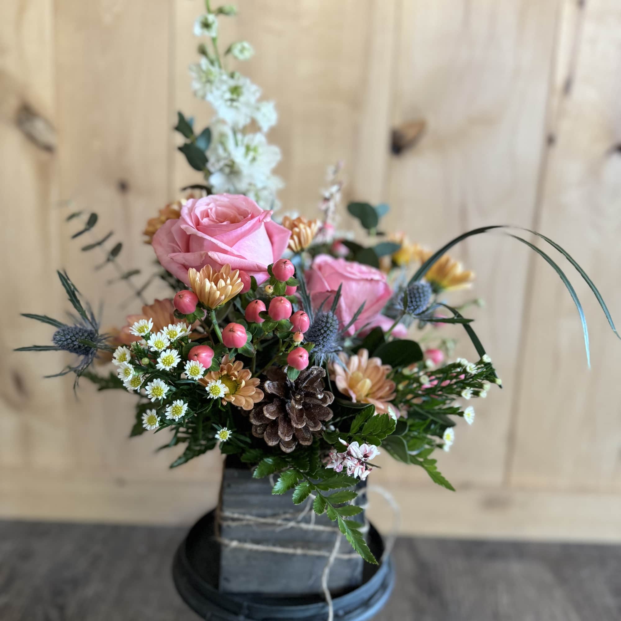 Pink roses and mixed flowers arranged in a square vase on a pedestal.