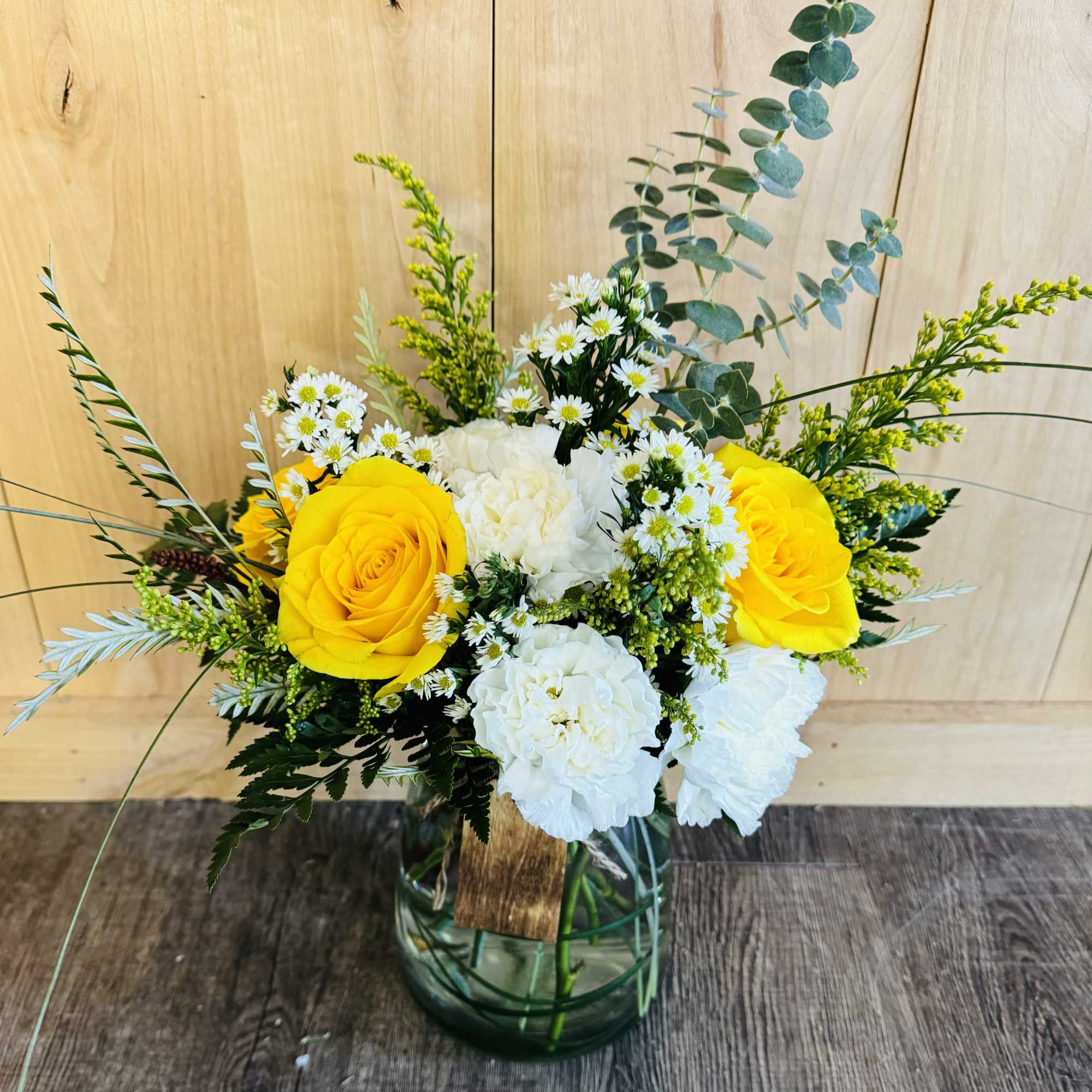 Yellow roses and white flowers in a glass vase with greenery