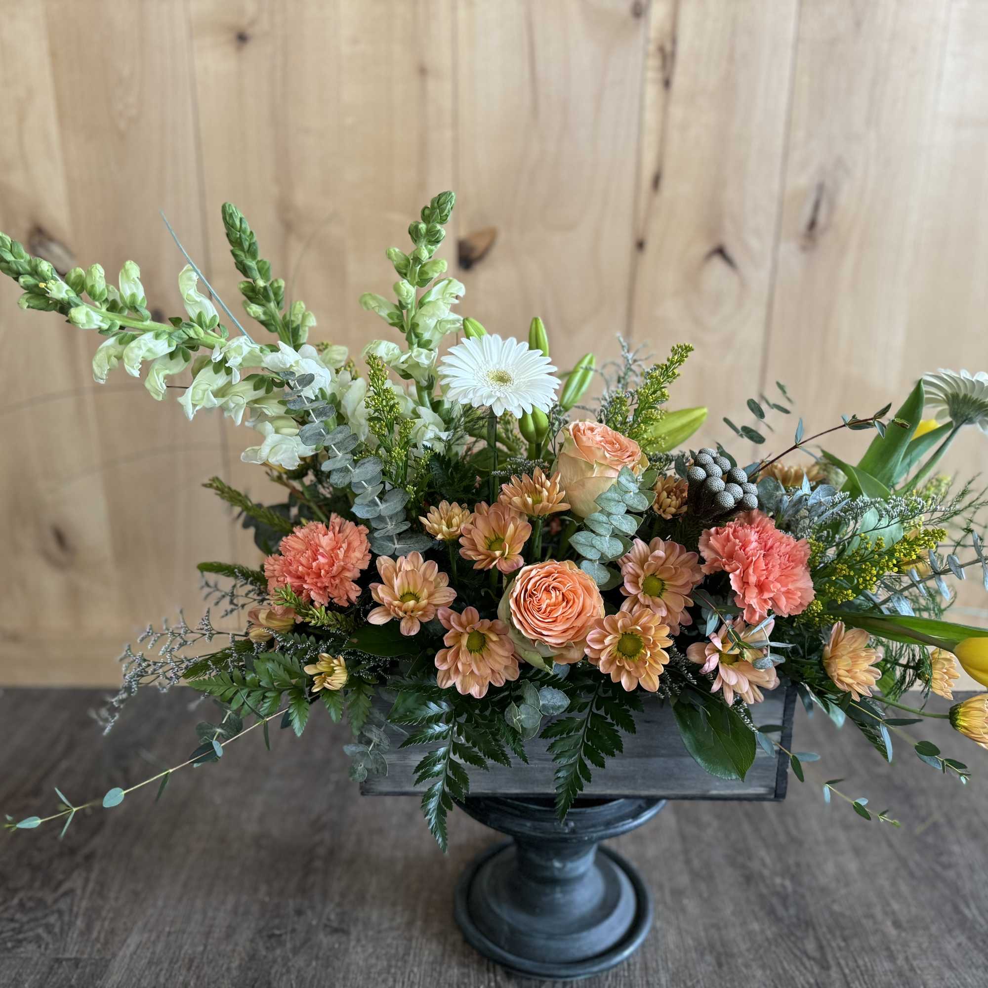 Mixed floral arrangement in a dark pedestal vase with peach, white, and yellow blooms
