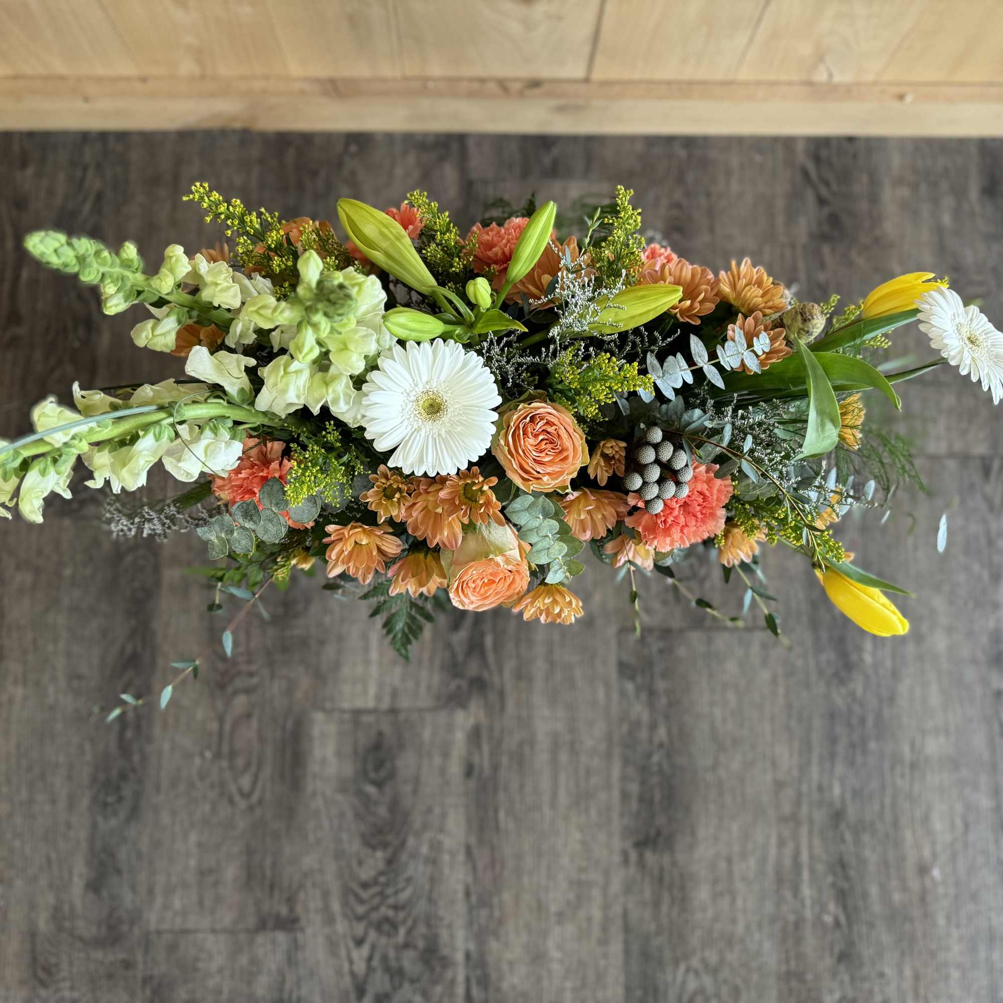 Long floral centerpiece with white daisies, orange roses, and lilies
