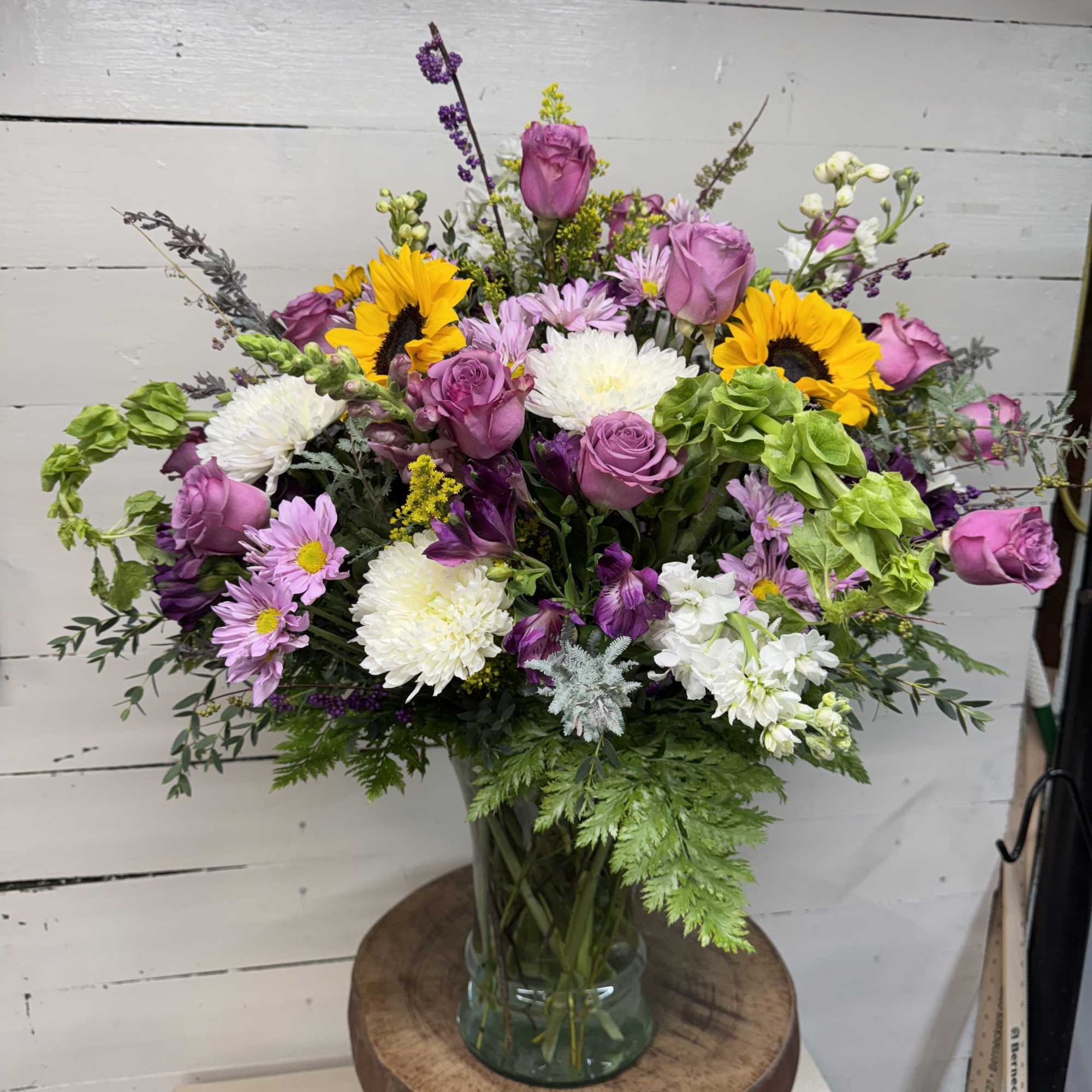 Mixed bouquet in a glass vase with pink roses, sunflowers, and white blooms