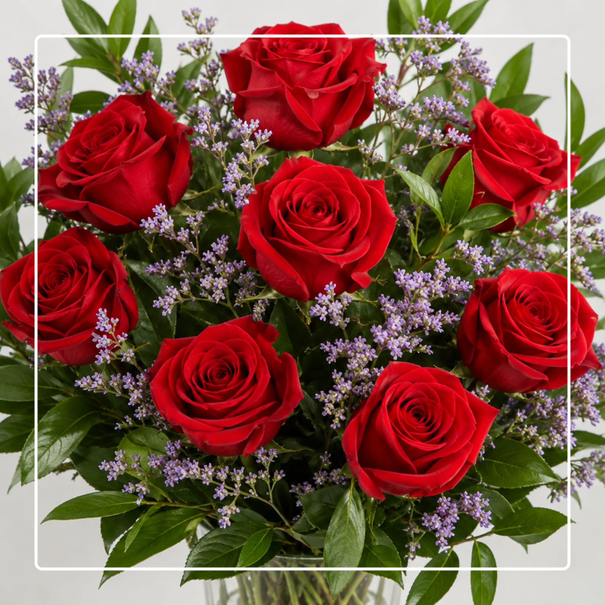 Bouquet of red roses with small purple filler flowers in a clear vase