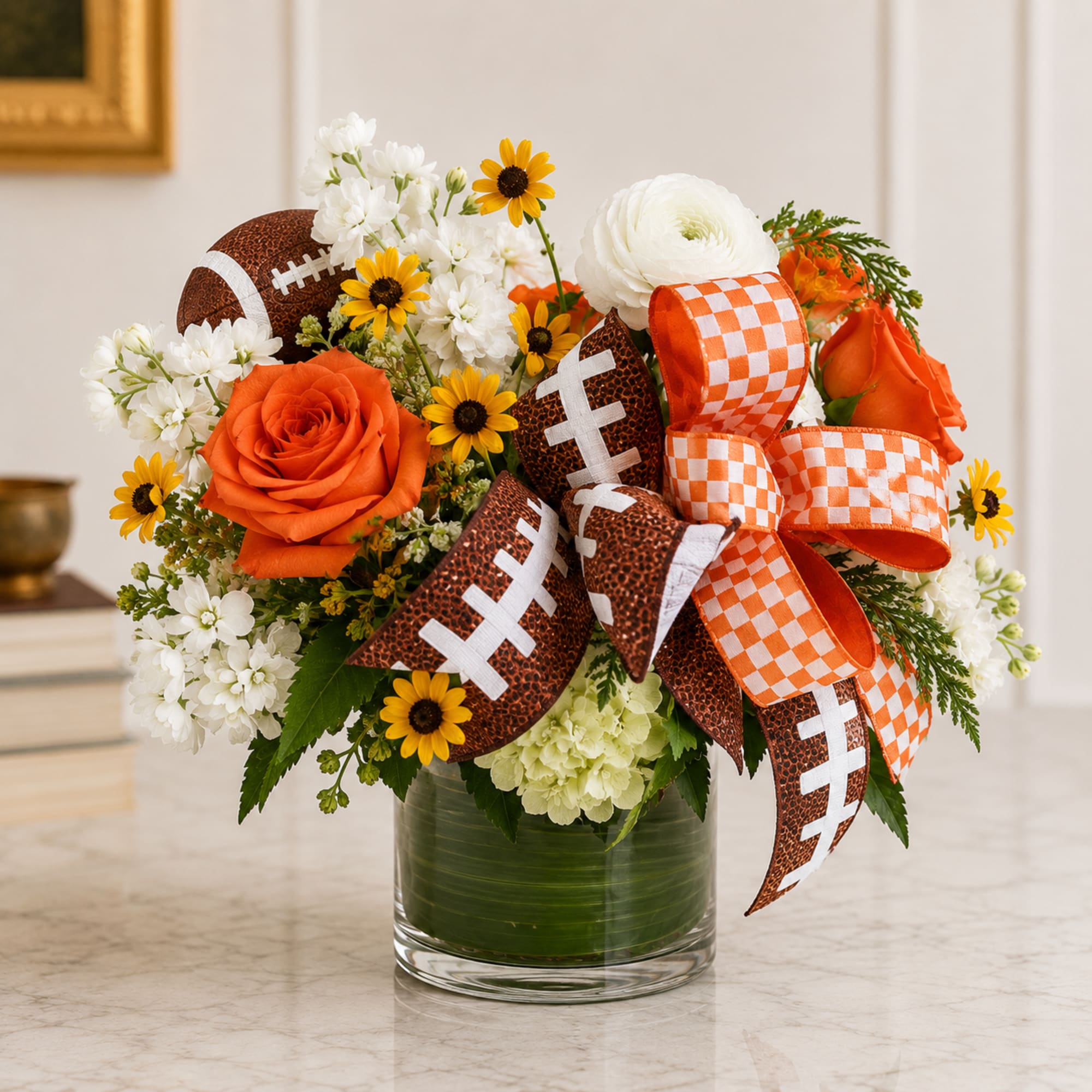 Orange and white floral arrangement in a glass vase with football ribbons
