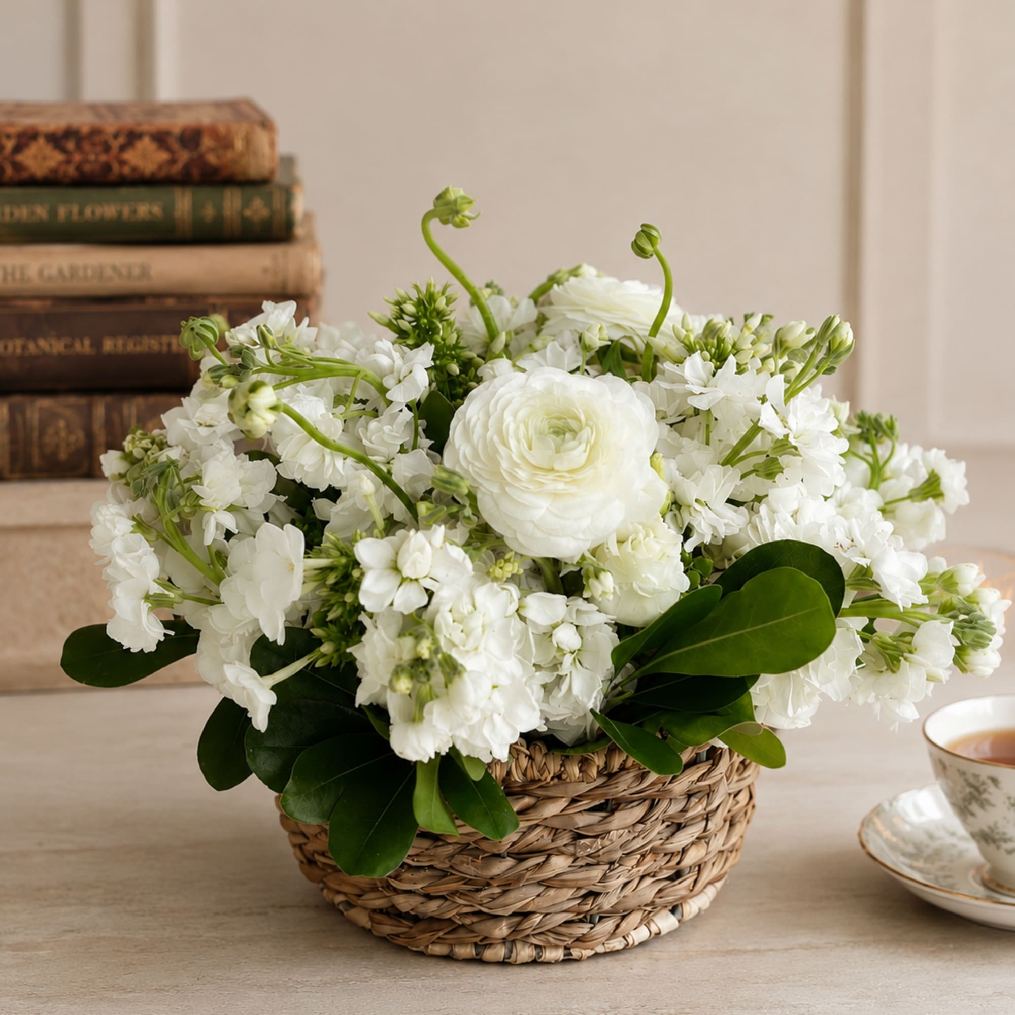 White floral arrangement in a woven basket with a teacup beside it