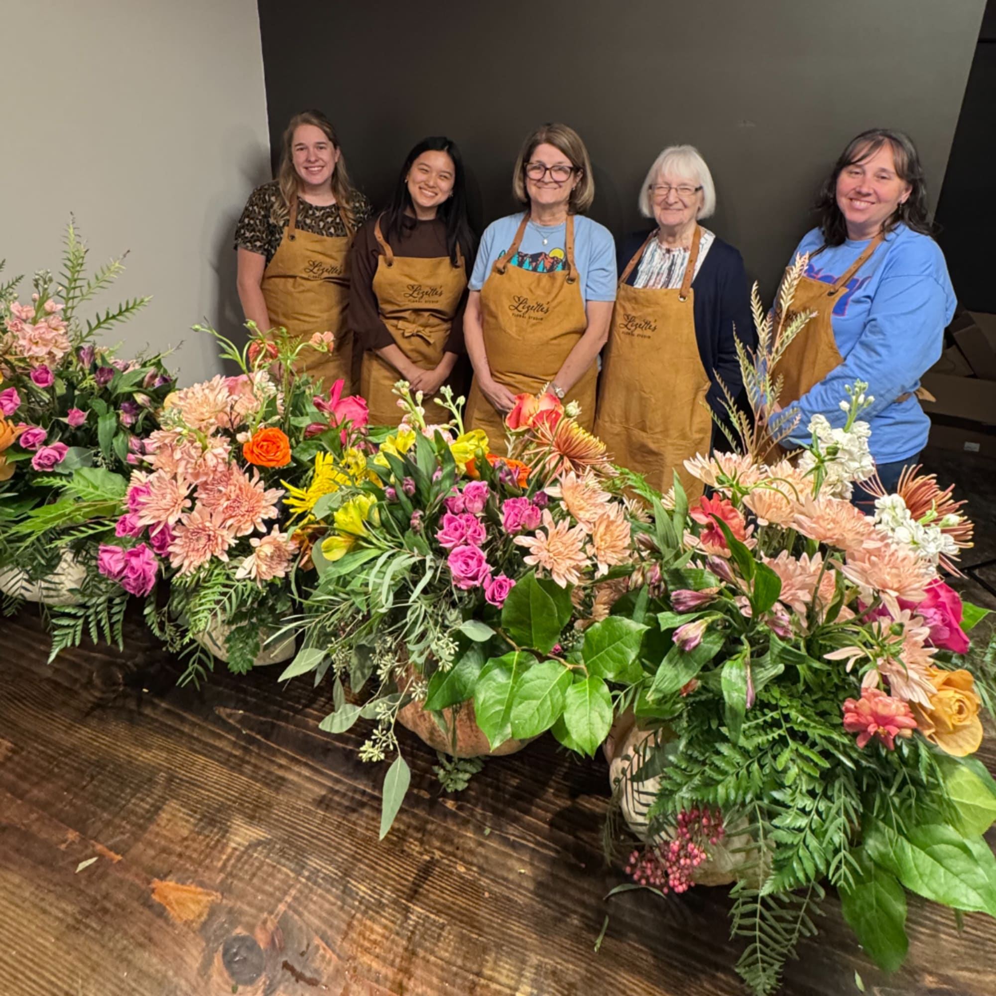 Group of women standing behind several colorful floral arrangements on a table