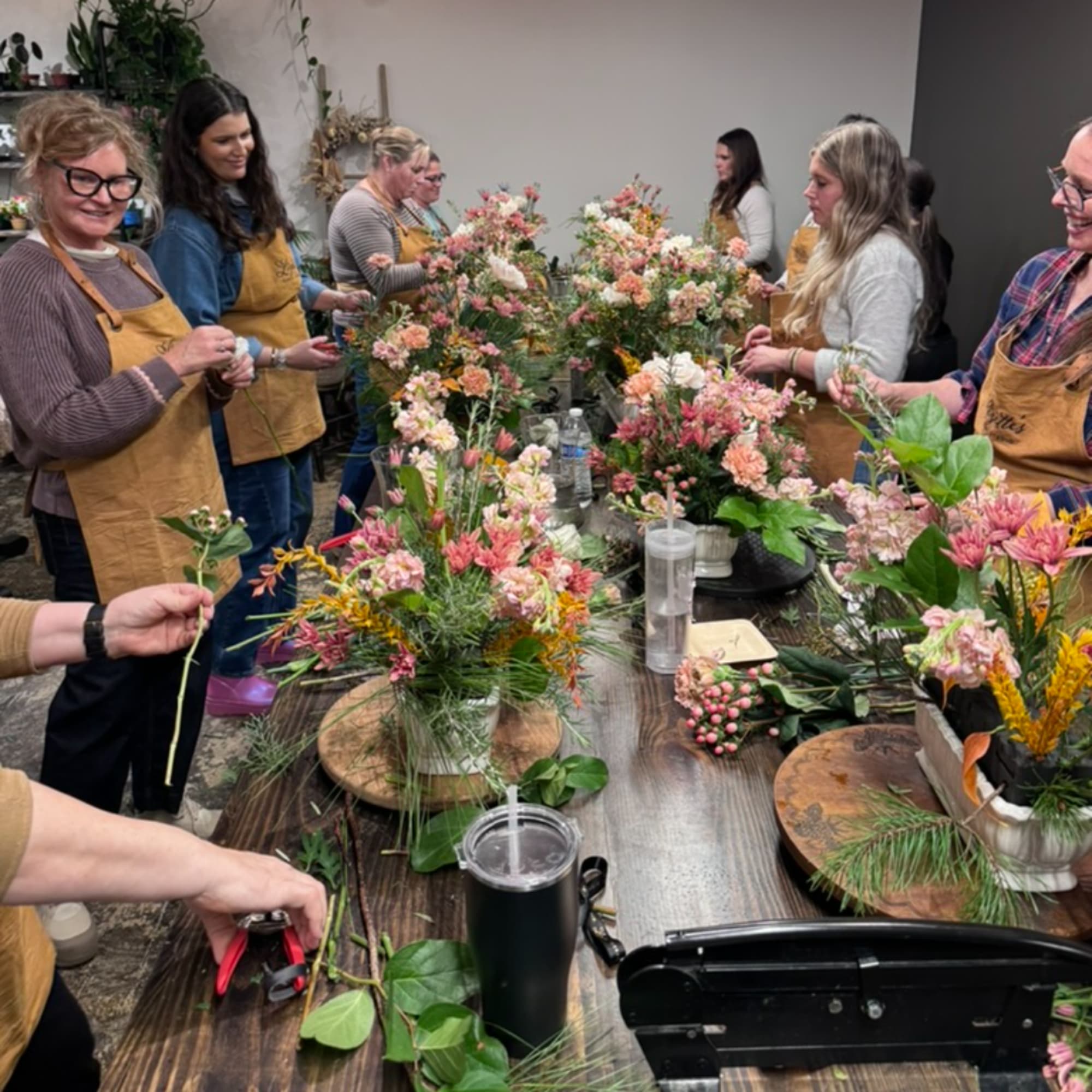 People arranging mixed flower bouquets around a table in a workshop