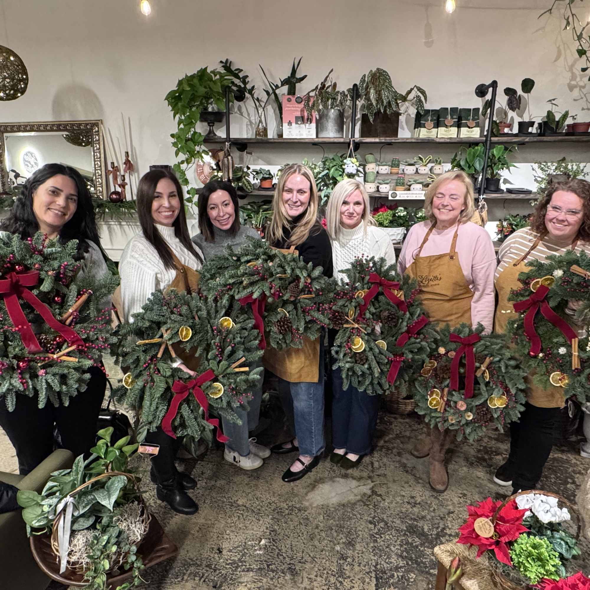 Group of women holding decorated evergreen wreaths in a flower shop