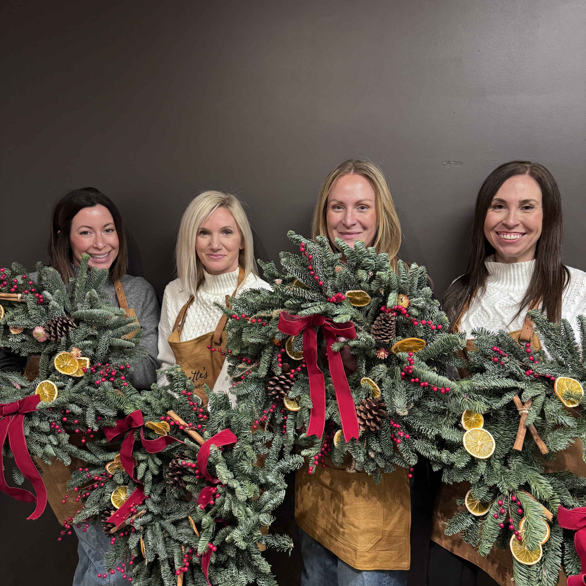 Women holding holiday wreaths with pine, berries, and ribbon