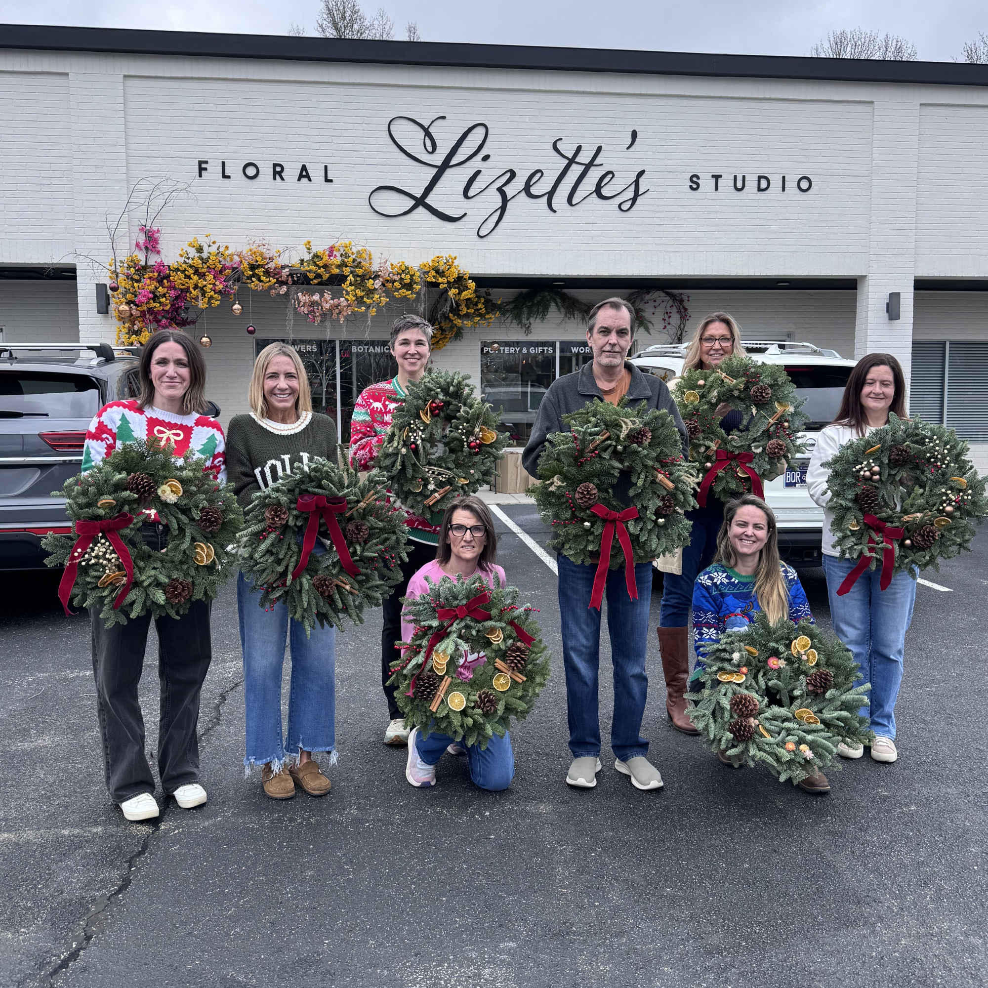 Group holding decorated evergreen wreaths outside a floral shop