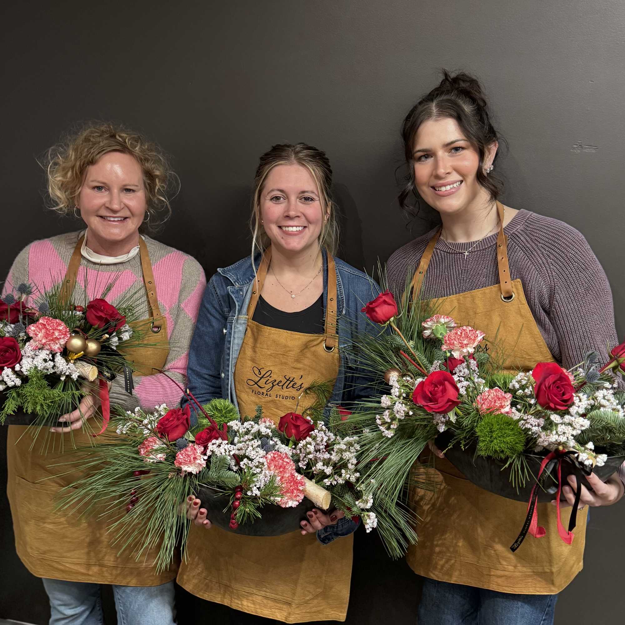 Three women holding holiday floral arrangements in shallow black containers
