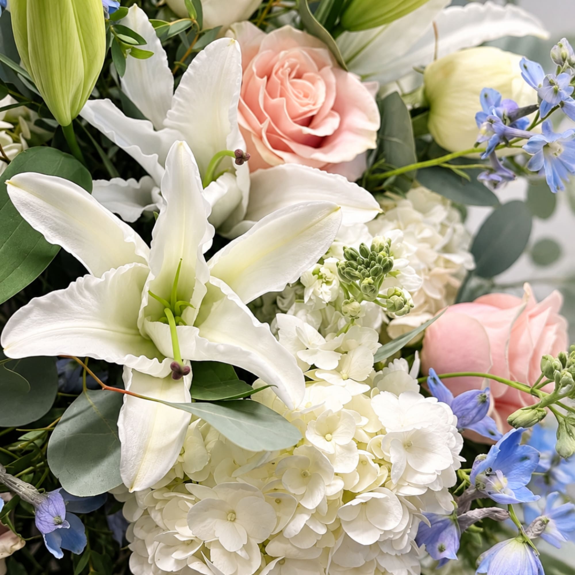 Bouquet with white lilies, pale pink roses, and blue flowers