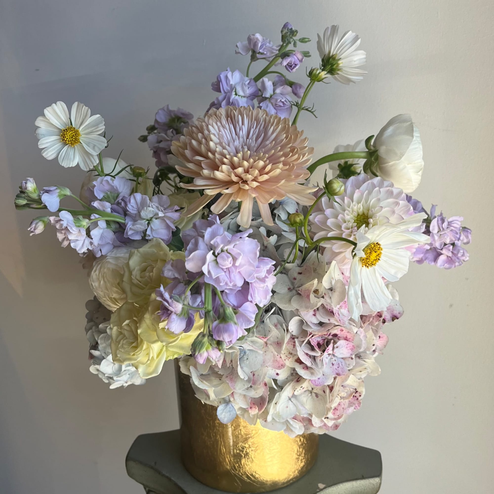 Pastel bouquet with white daisies, lavender blooms, and a gold vase