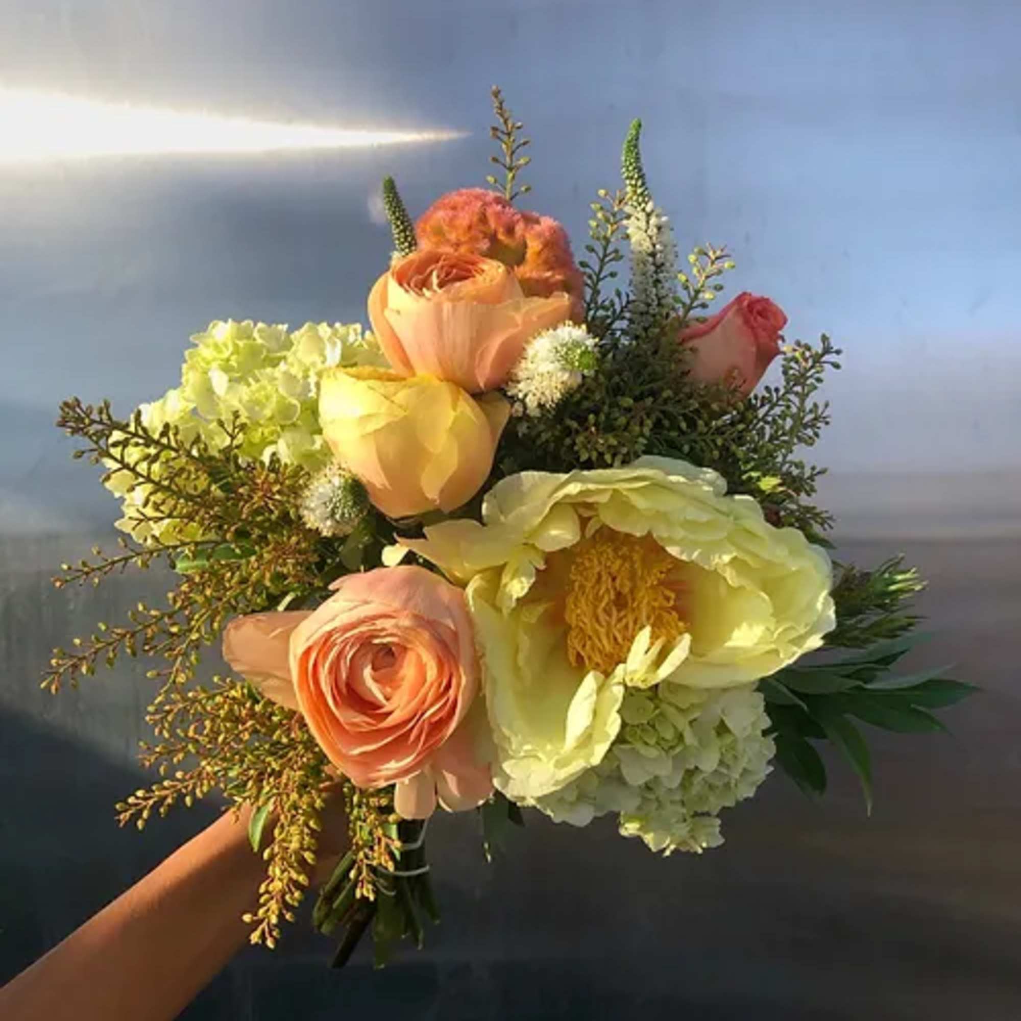 Handheld bouquet of peach and yellow roses with white blooms