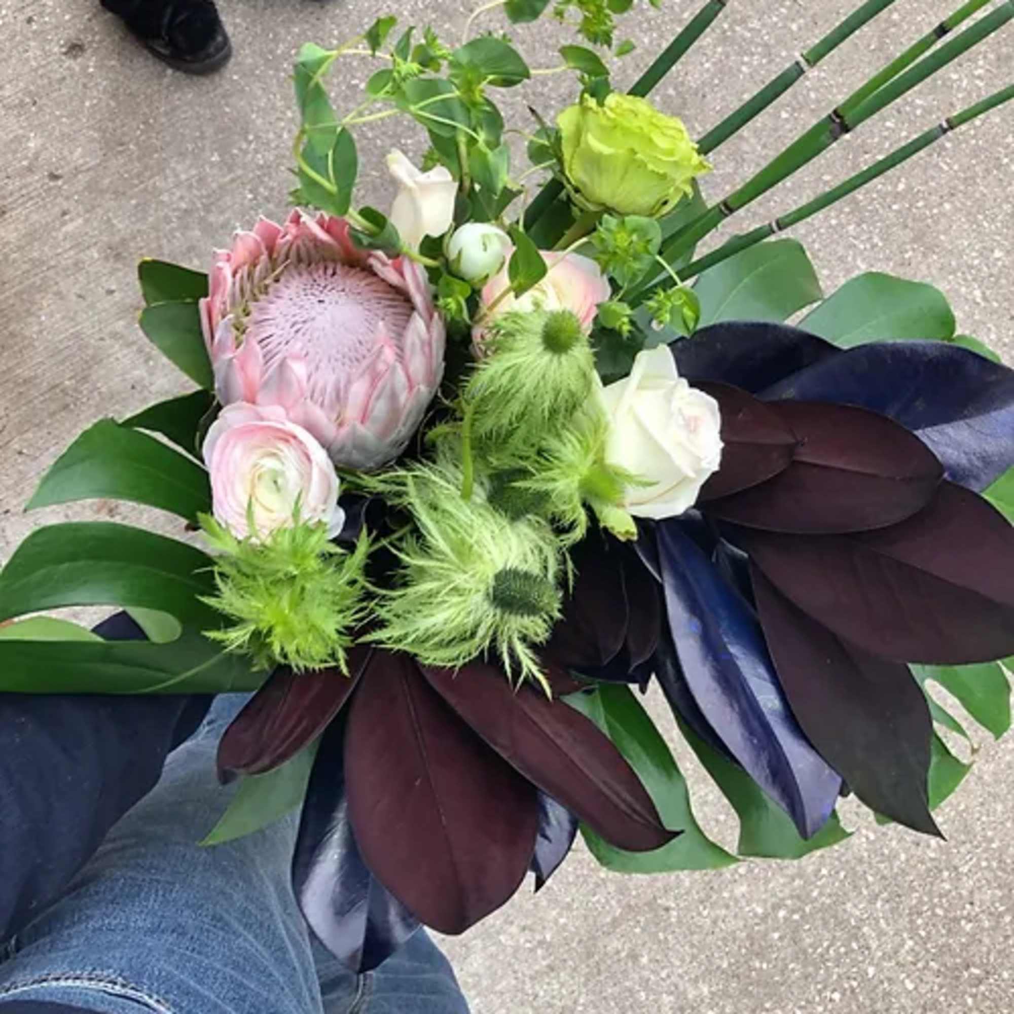 Handheld bouquet with a pink protea, white roses, and green accents