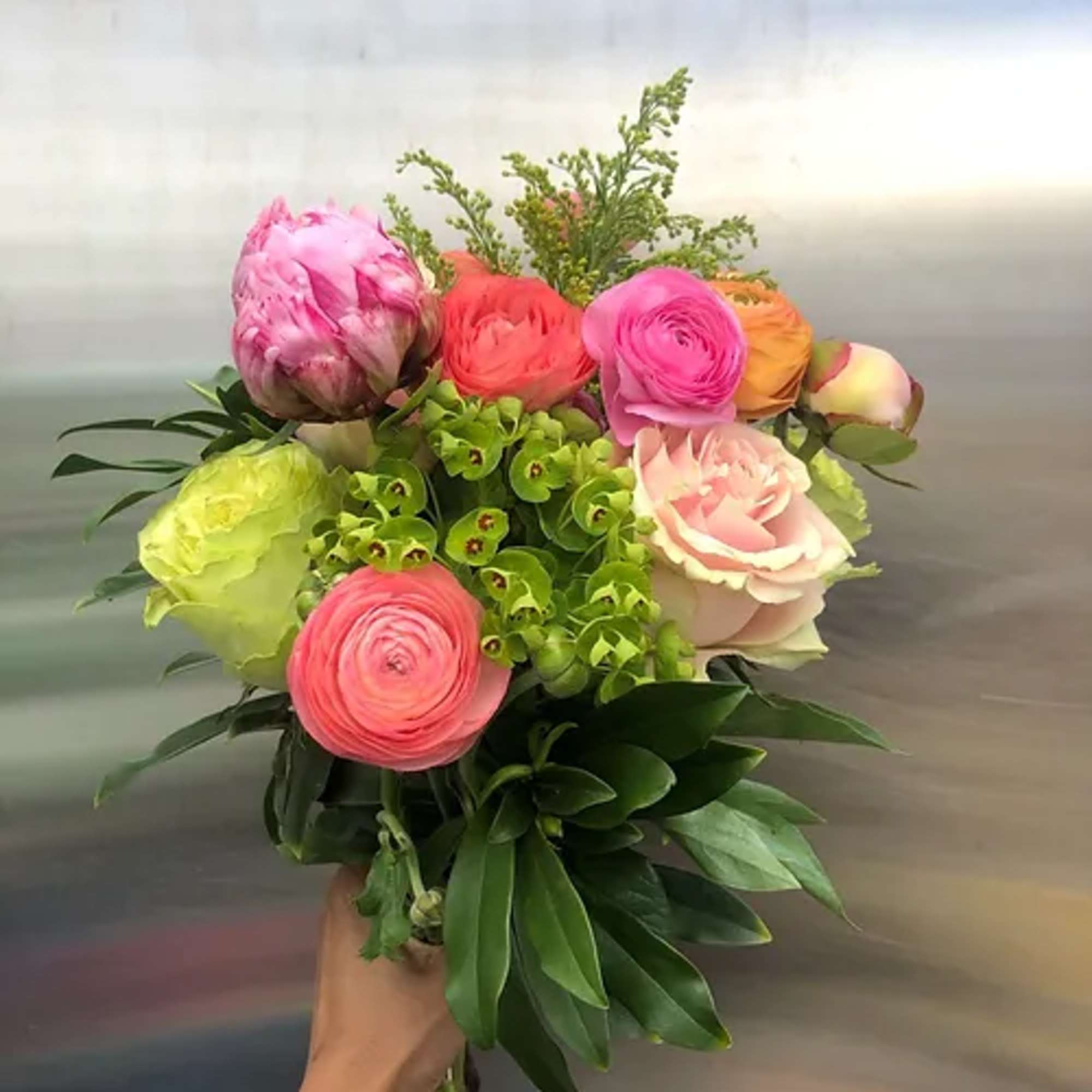 Handheld bouquet of pink, coral, and green blooms with leafy accents