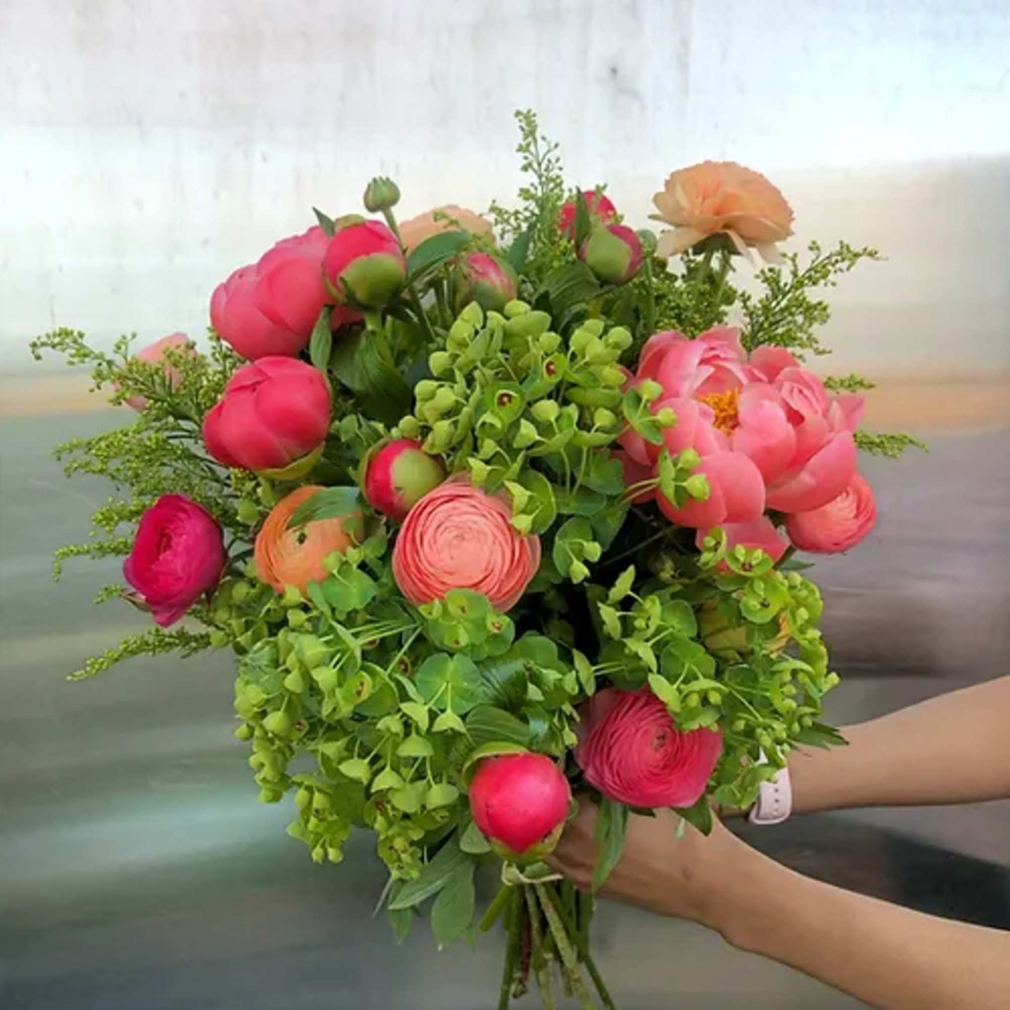 Handheld bouquet of pink and peach flowers with lush greenery