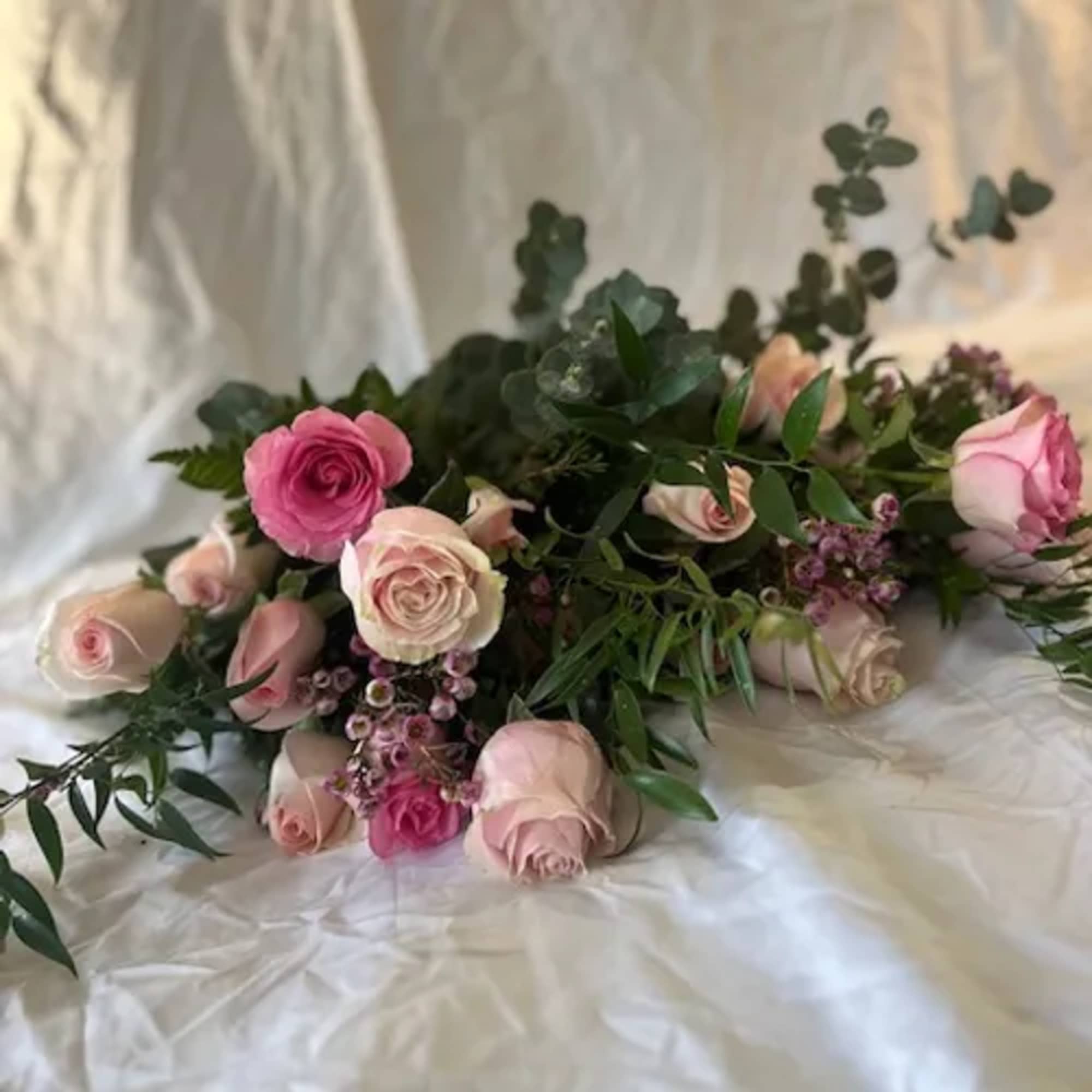 Pink and blush roses arranged with greenery on white fabric