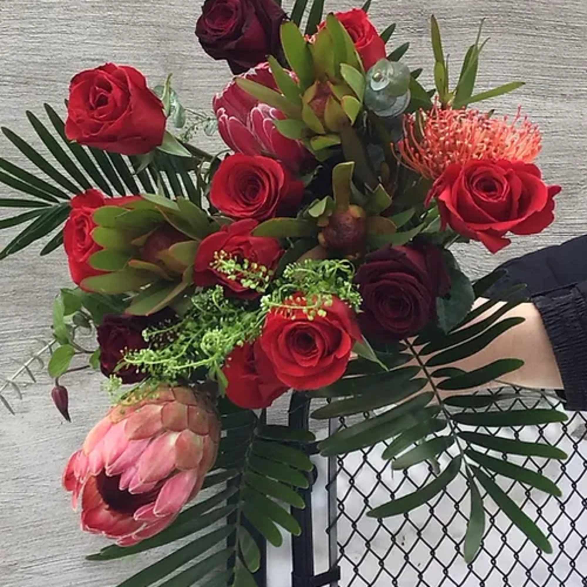 Bouquet of red roses and pink protea with palm fronds