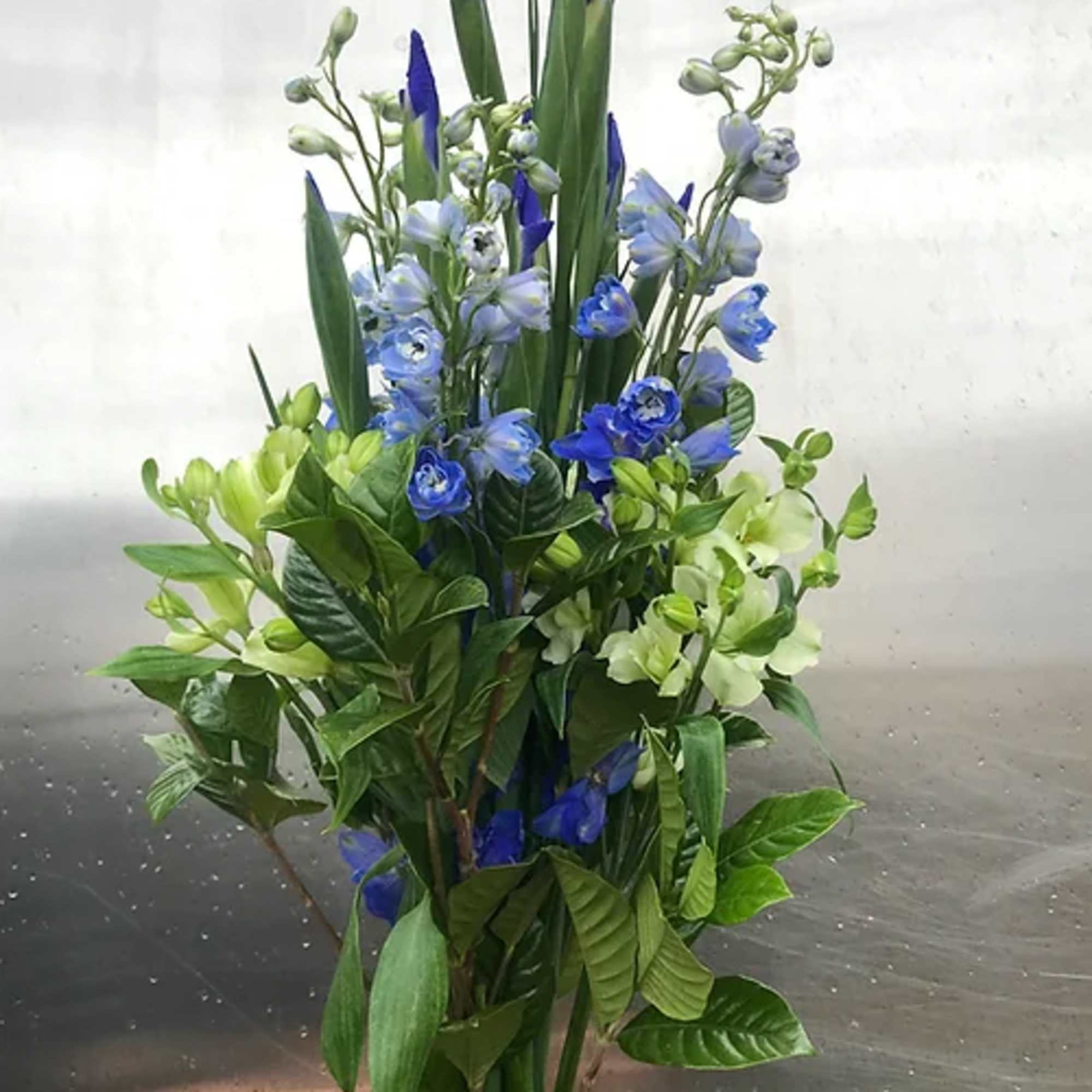 Tall bouquet of blue and pale green flowers held by two hands