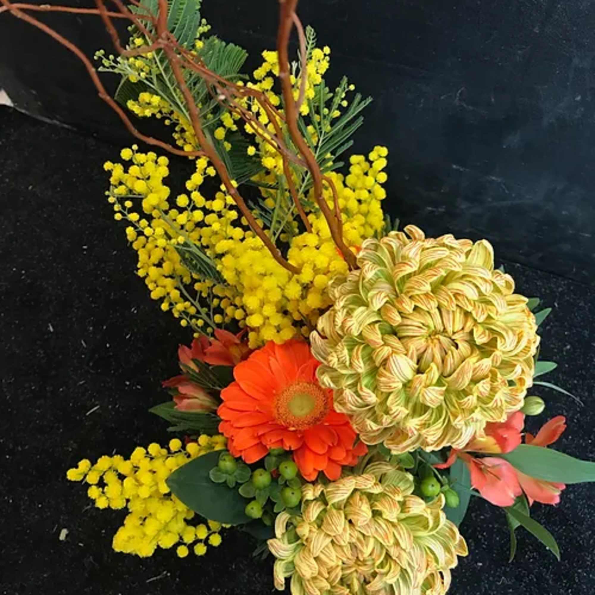 Orange gerbera daisies with yellow blooms and branches in a floral arrangement