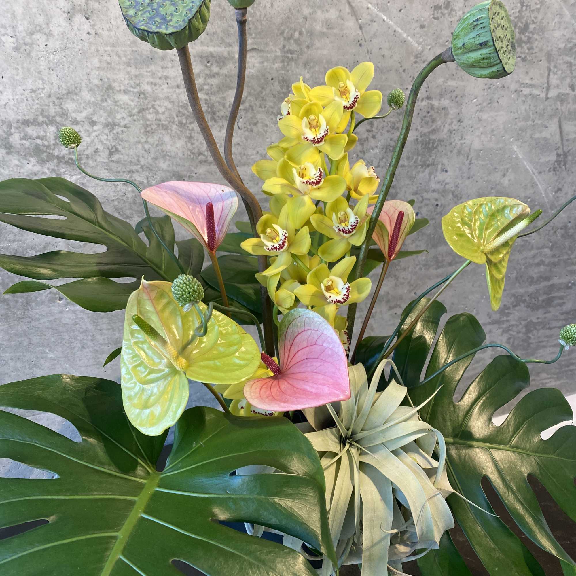 Tropical arrangement with yellow orchids, anthuriums, and lotus pods