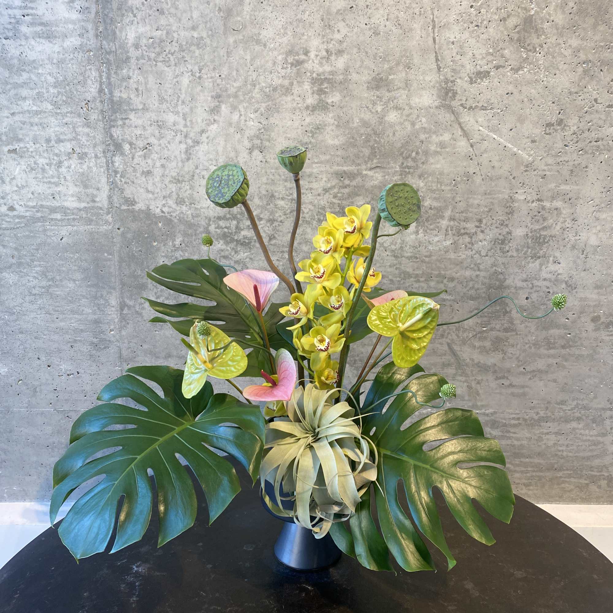 Tropical arrangement with yellow orchids and large monstera leaves in a vase