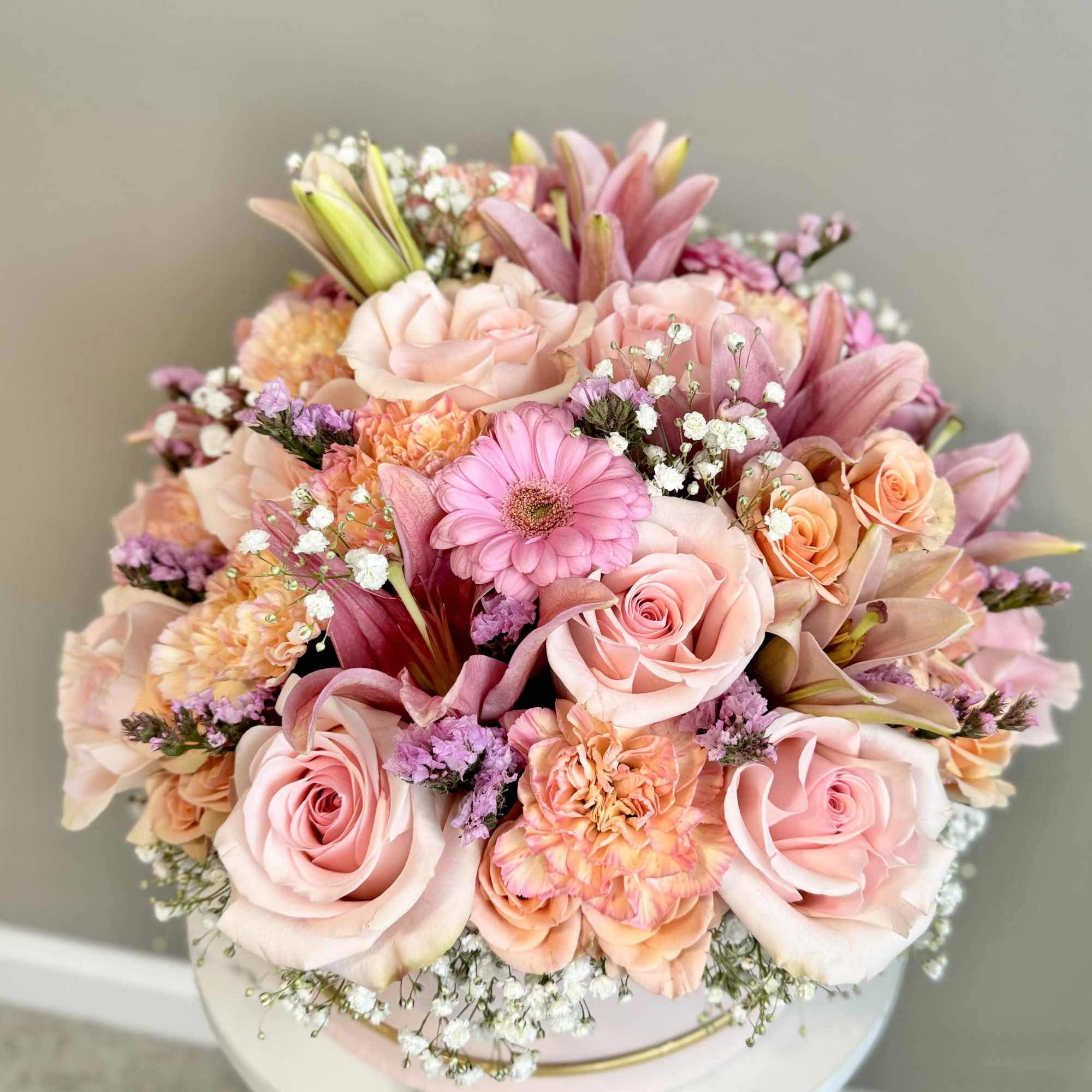 Pink and peach bouquet with roses, lilies, and a gerbera daisy in a round box