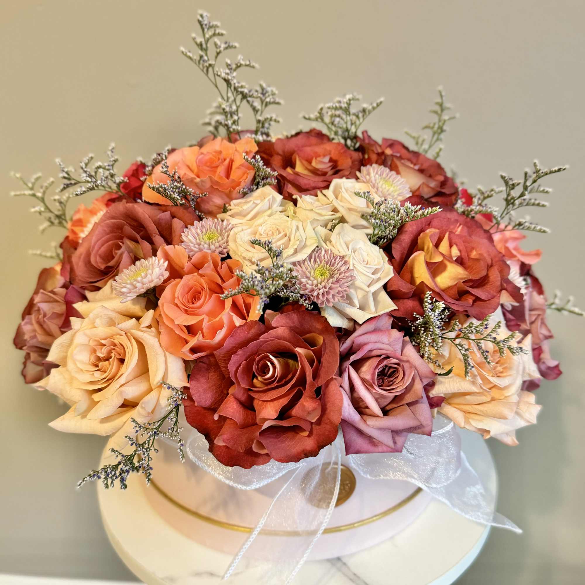 Bouquet of roses in peach, red, and pink with a white ribbon