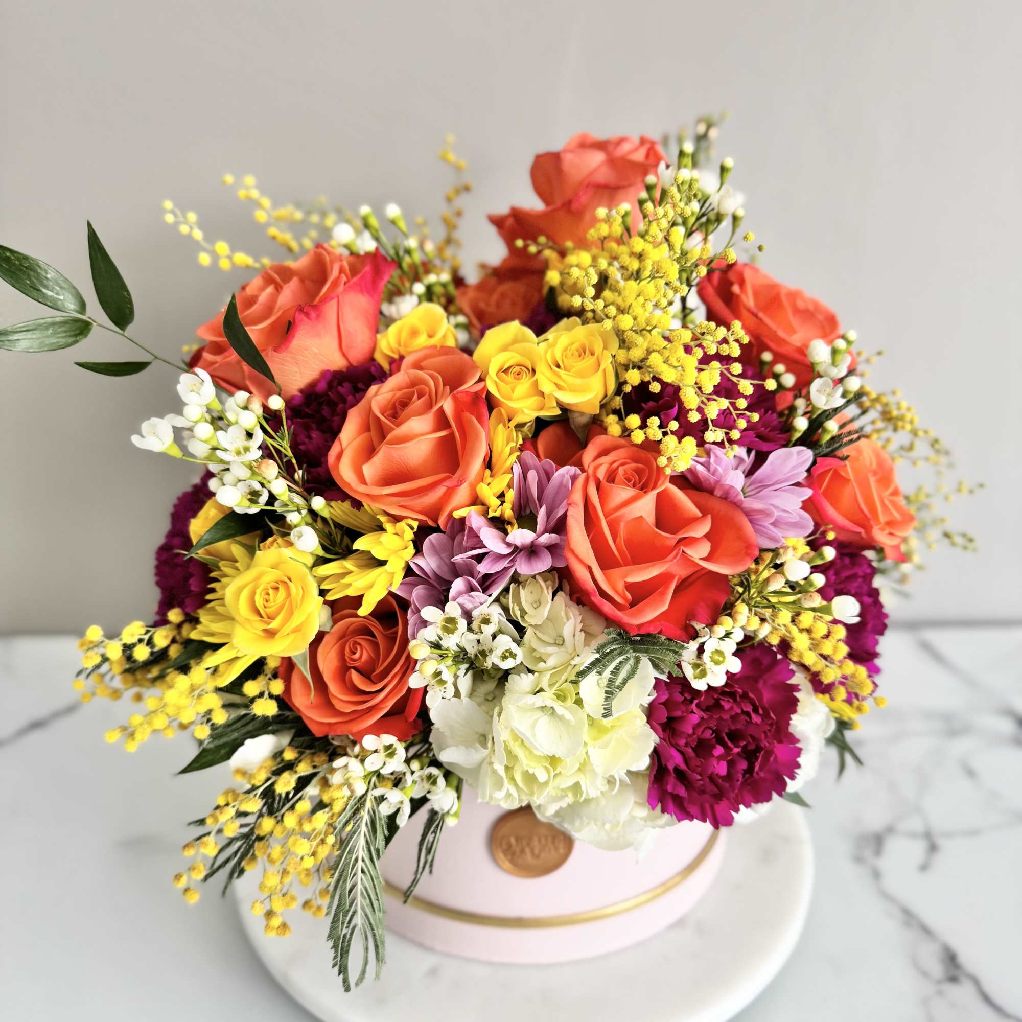 Mixed bouquet of roses, carnations, and yellow filler flowers in a pink hat box