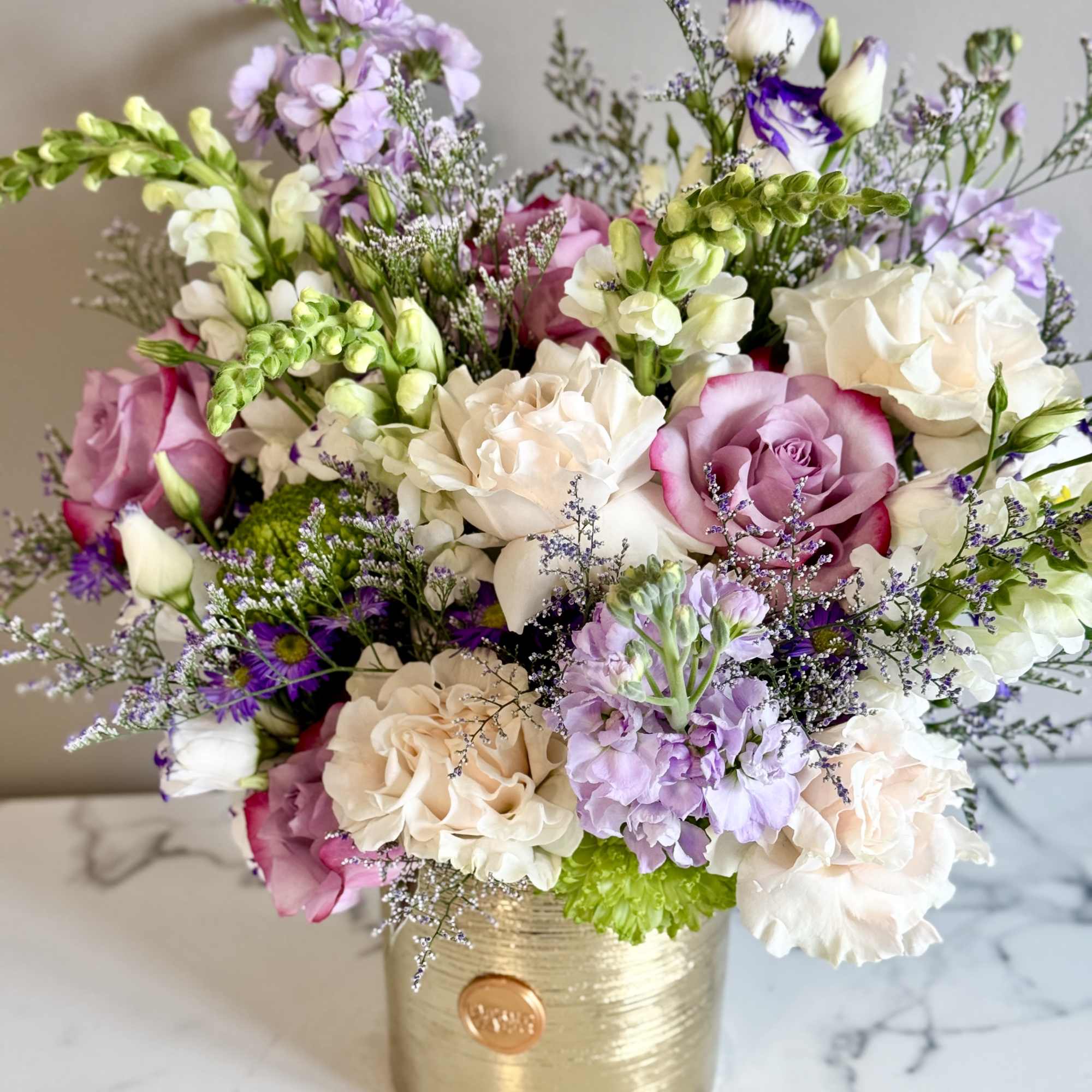 Mixed arrangement of purple, pink, and white flowers in a gold cylinder vase
