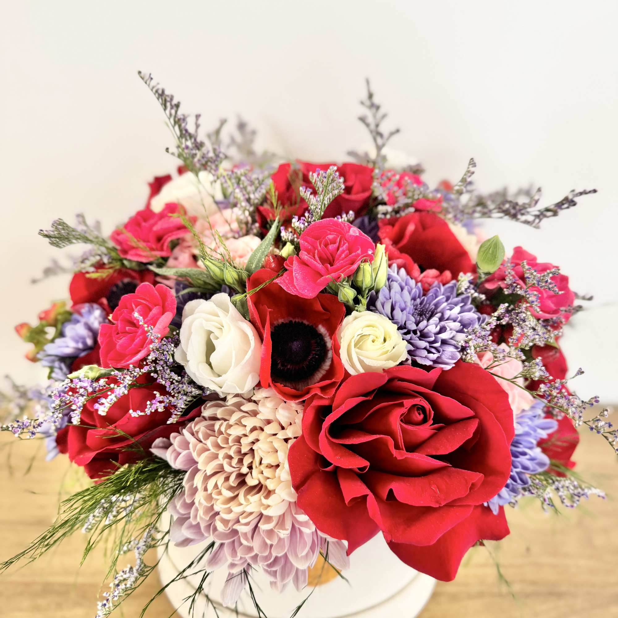Mixed bouquet of red, pink, white, and lavender flowers in a white box